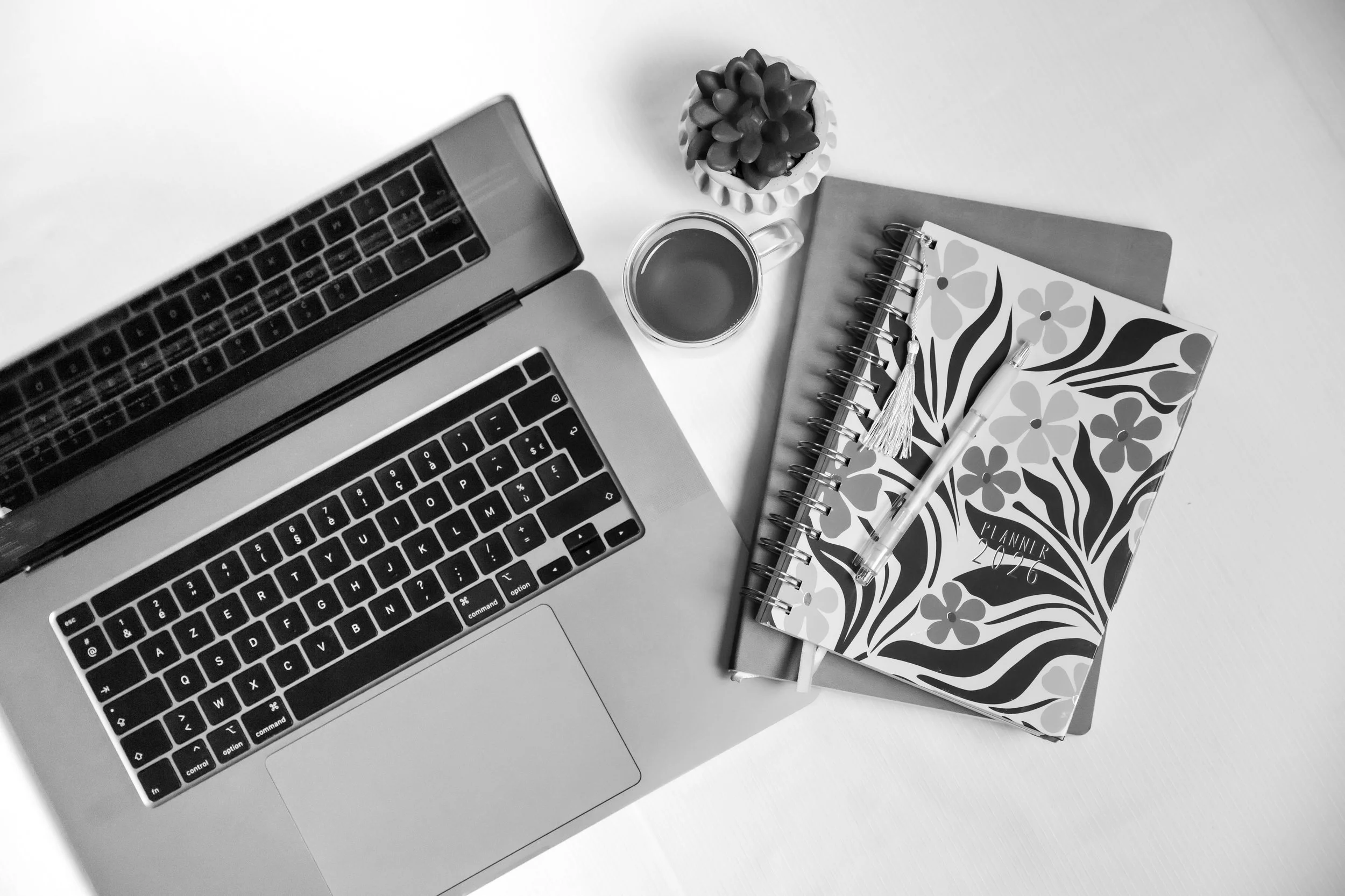 Ordinateur portable, une tasse de café, un carnet avec floral design, un stylo, une petite plante