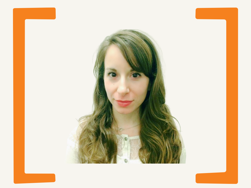 A young woman with long, wavy brown hair and fair skin, wearing a white lace top and a delicate necklace, looking at the camera.