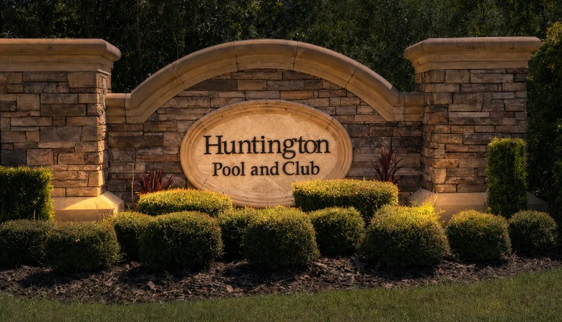 A stone and brick sign reads 'Huntington Pool and Club' and is surrounded by well-maintained shrubs and landscaping.