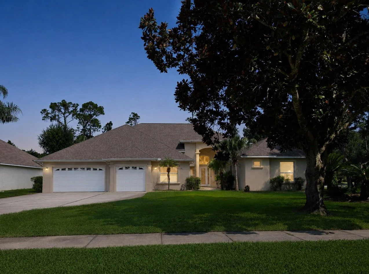 A suburban house during twilight with a manicured lawn, large trees, and a two-car garage.