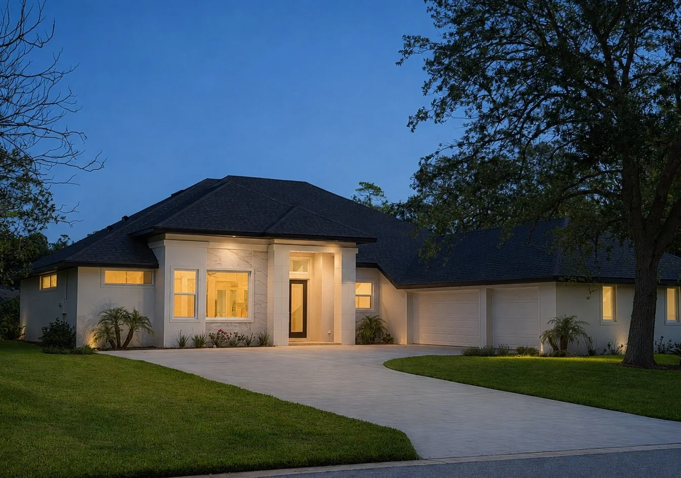 Modern house at dusk with large front yard, driveway, and illuminated windows.