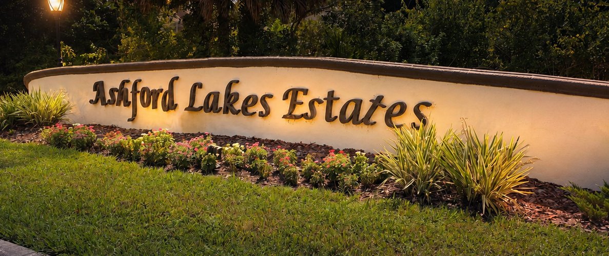 Entrance sign for Ashford Lakes Estates surrounded by landscaped plants and flowers at night.