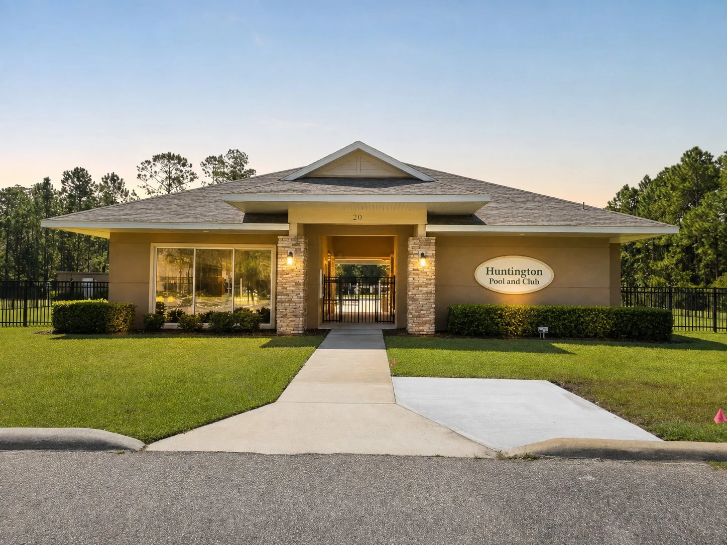 Front view of a building with a sign that reads 'Huntington Pool and Club', surrounded by green grass and trees, with a sidewalk leading to the entrance.