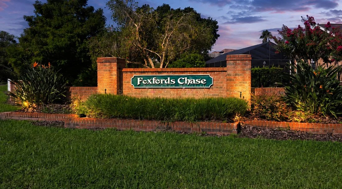 Entrance sign for Foxfords Chase neighborhood, brick wall with landscaping and trees in the background, evening lighting.