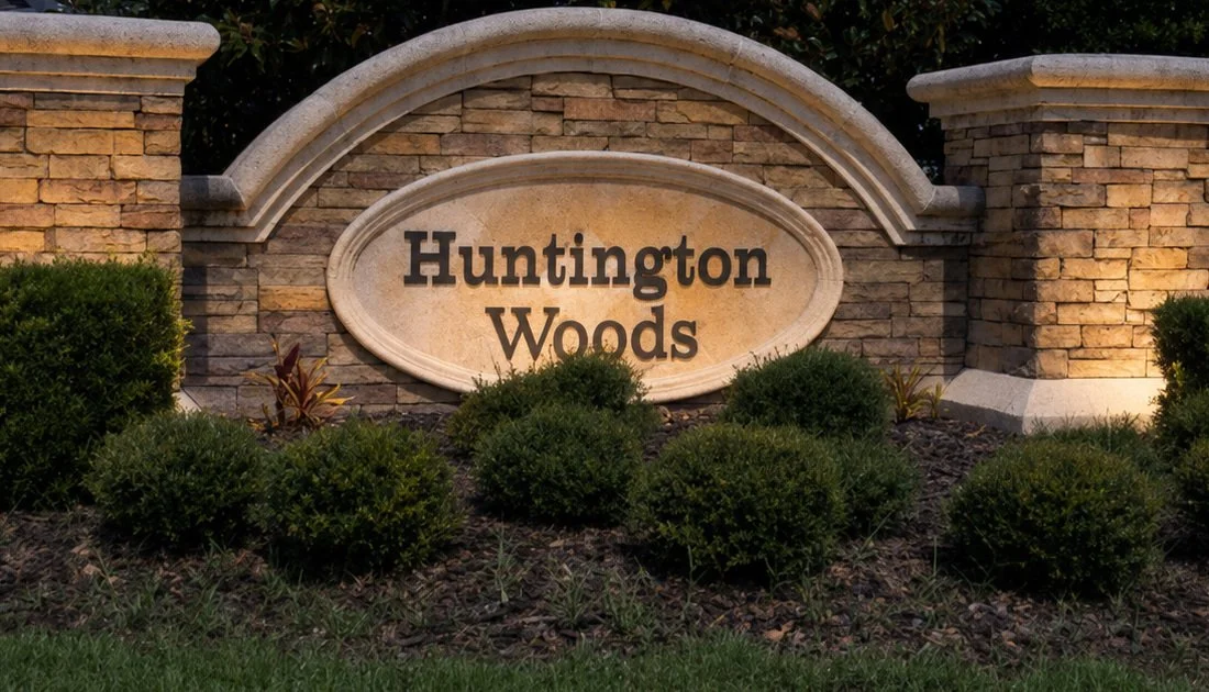 Stone sign reading 'Huntington Woods' surrounded by bushes and brick pillars.