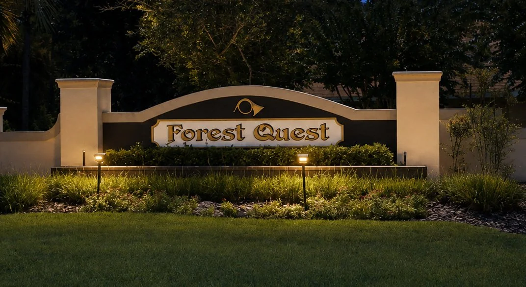 Entrance sign for Forest Quest community, illuminated at night, with landscaped greenery and pathway lights.