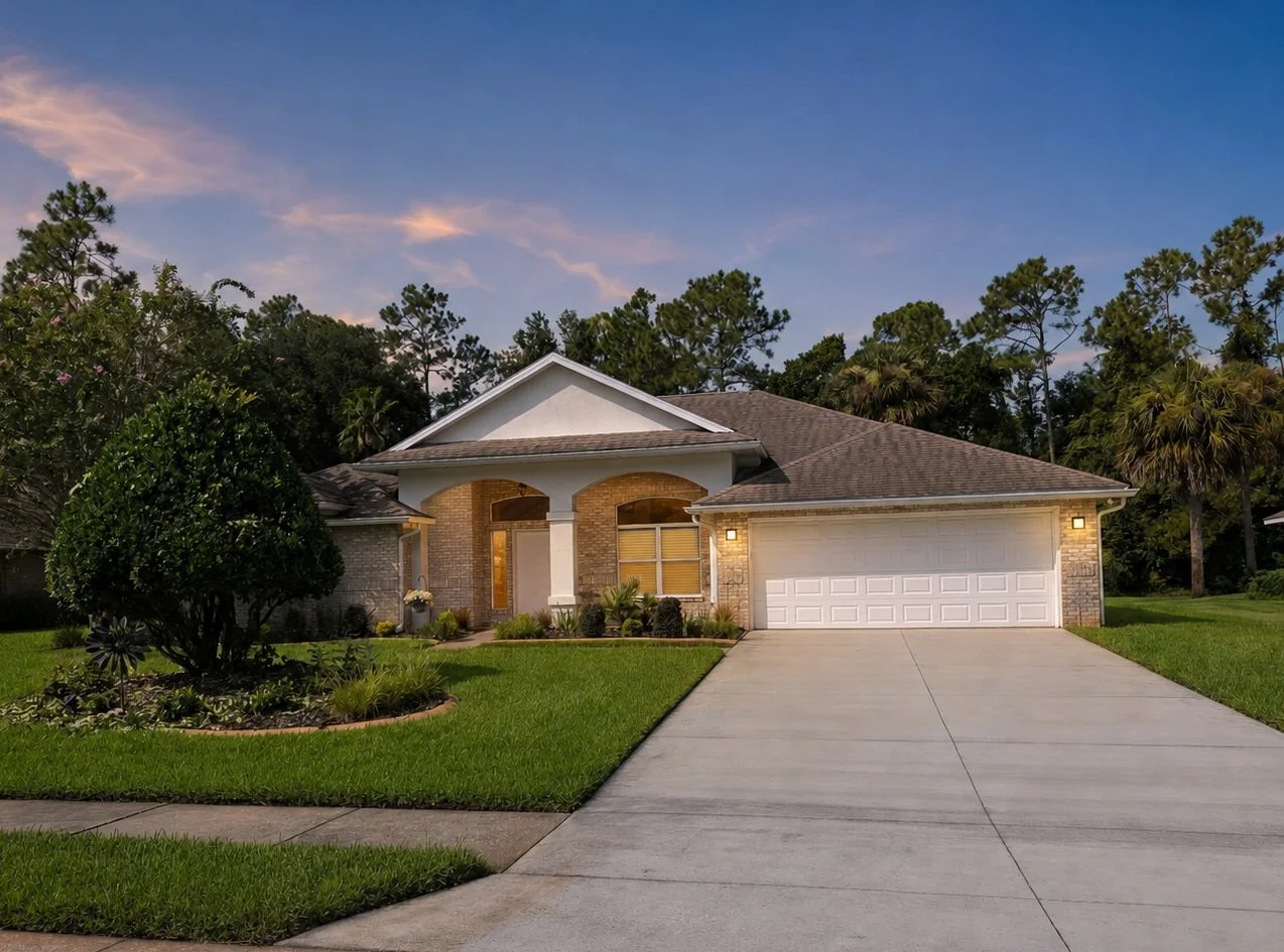 Front view of a modern suburban house with a driveway, well-maintained lawn, and trees under a clear evening sky.