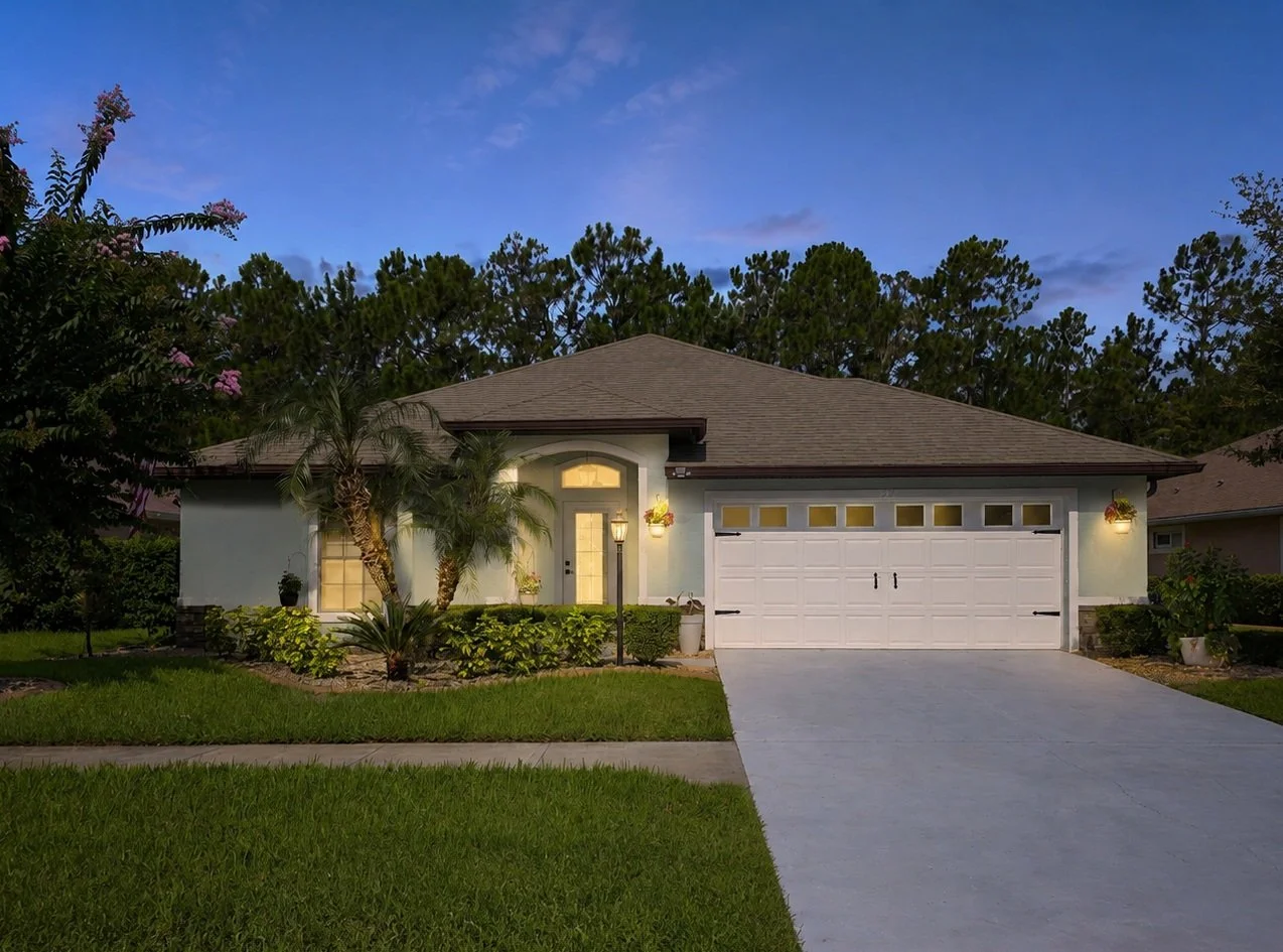 A modern single-story house with a white garage door, front porch, and landscaped yard at dusk.