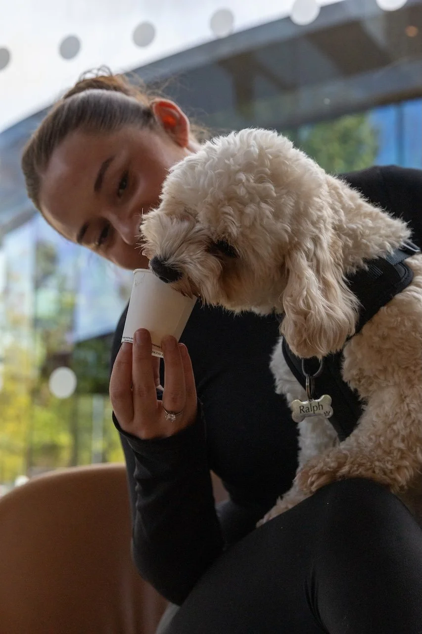A young woman holding a white puppy with long ears close to her face, smoking a cigarette in a casual indoor setting.