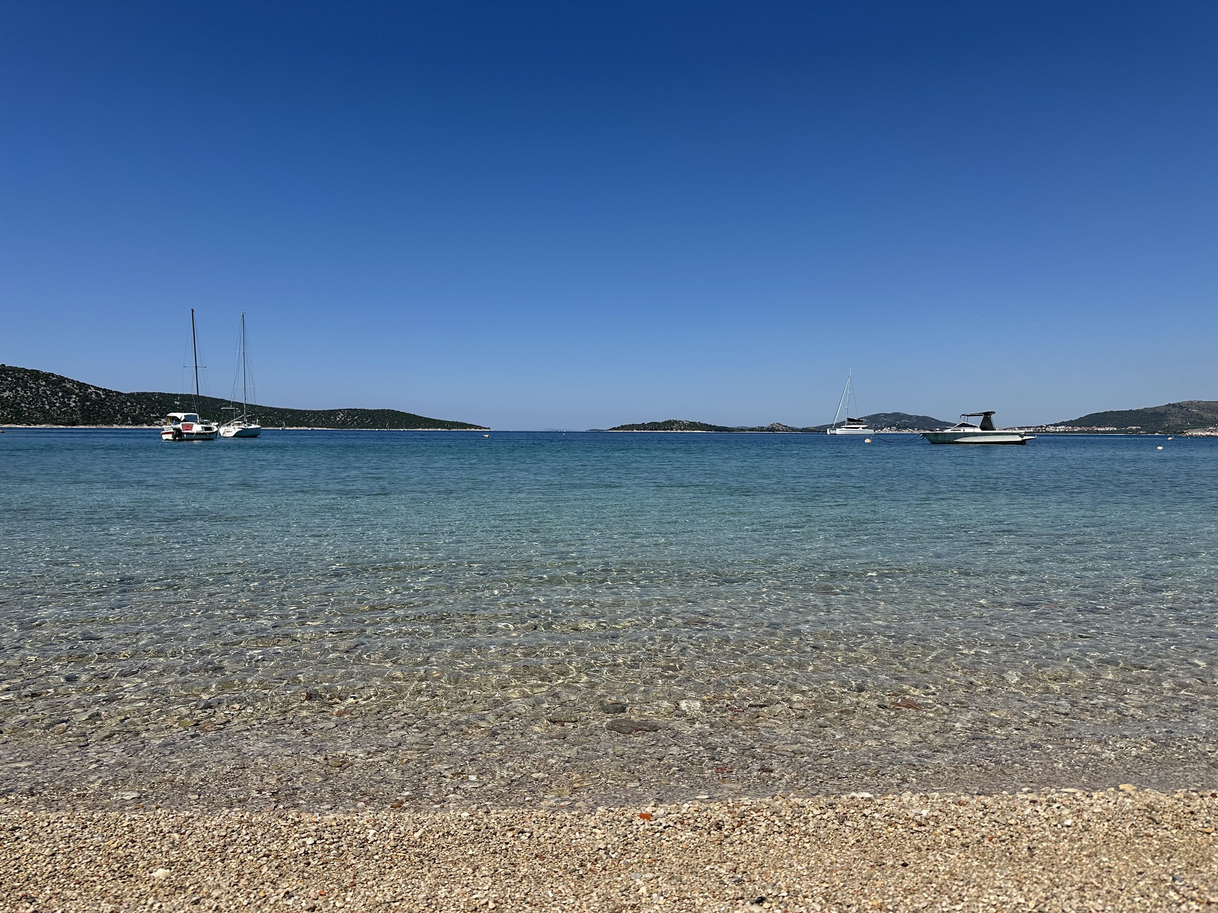 Calm open water with boats anchored in the distance under a clear blue sky