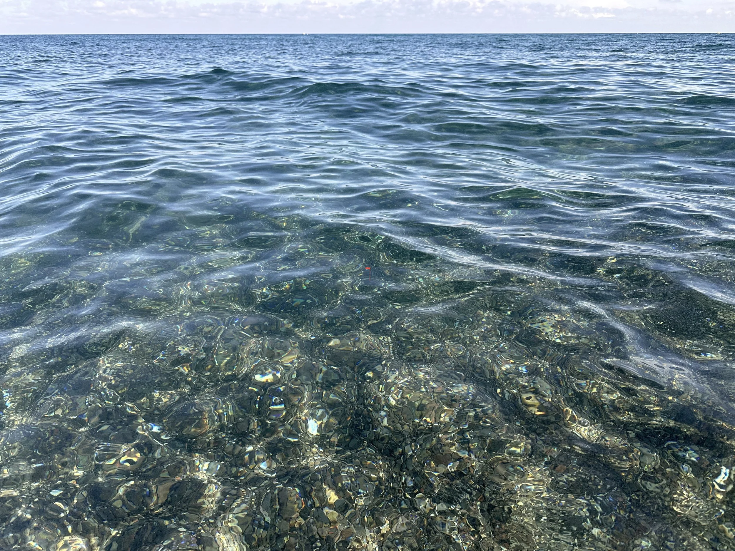 Clear open water with sunlight reflecting on rippling surface and visible stones beneath.