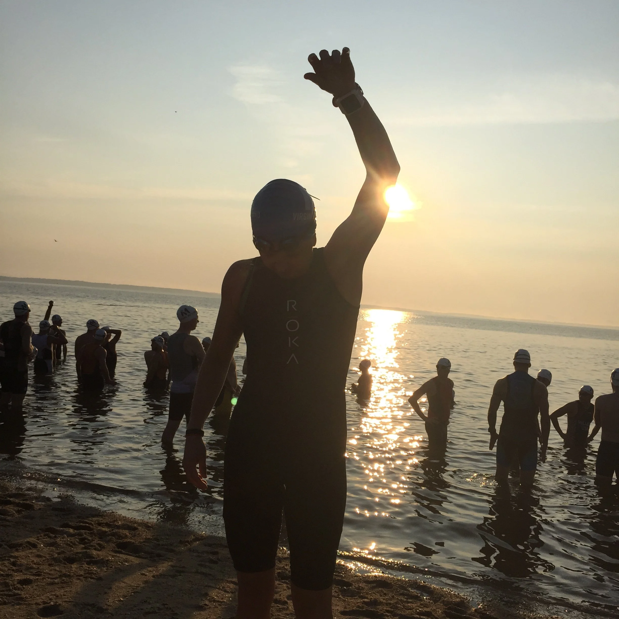 Open water swimmer warming up on the beach before a triathlon, wearing a swim skin in moderate water conditions