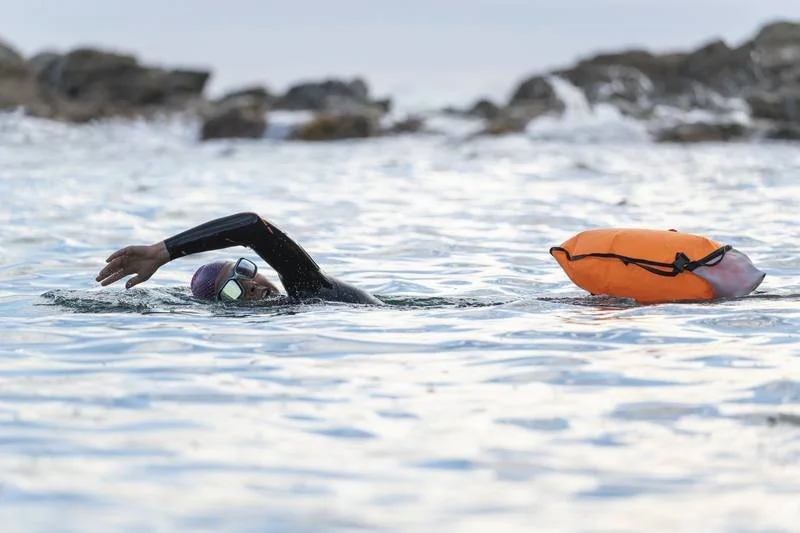 “Open water swimmer using a safety buoy in calm conditions”