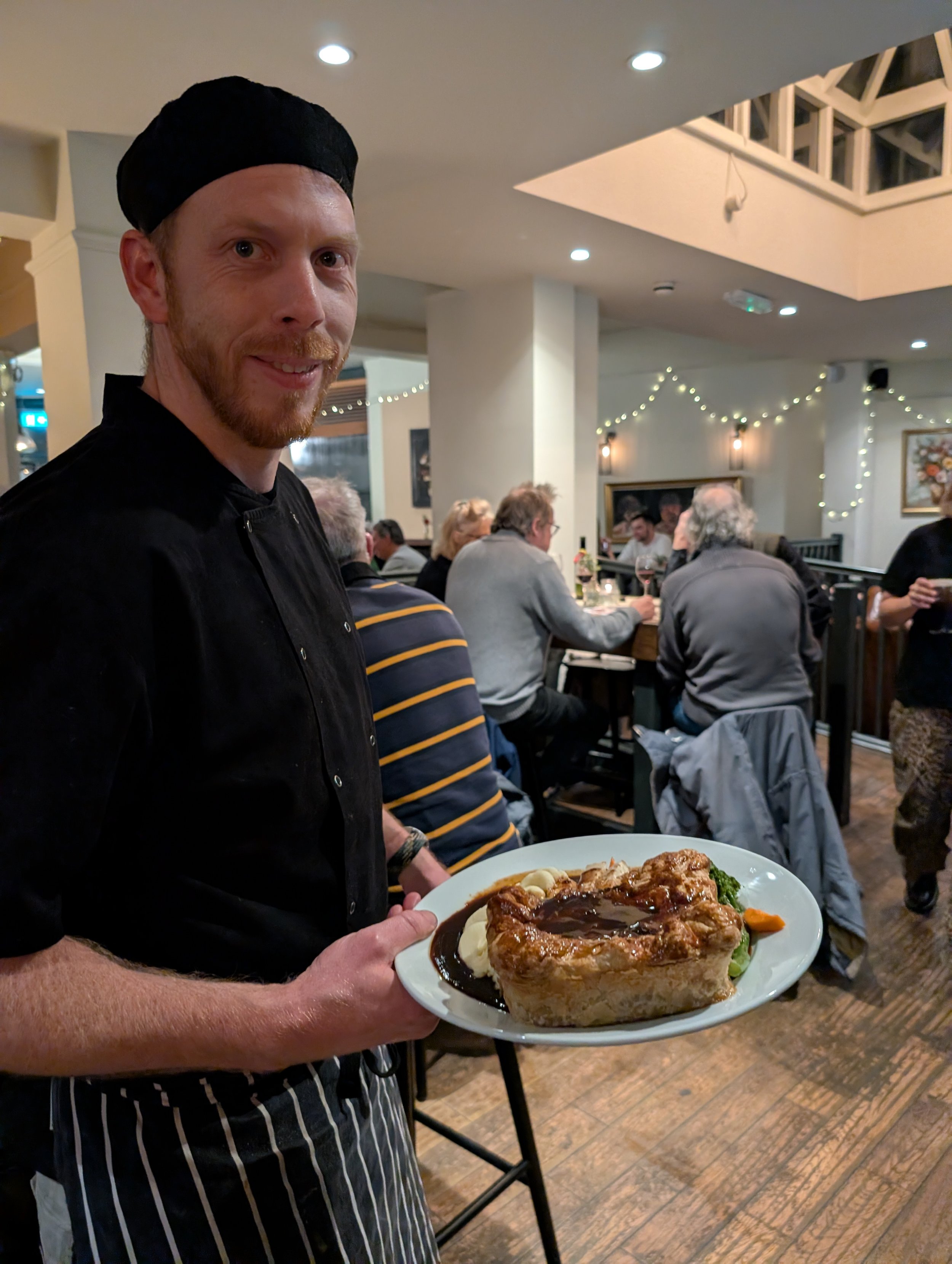 Chef holding a plate of meat pie in a busy restaurant