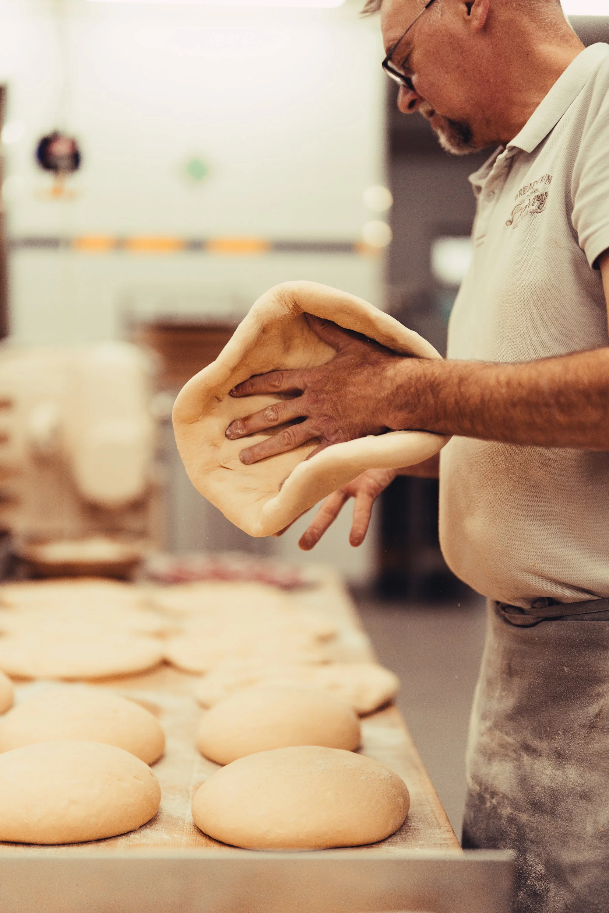 Ein Mann formt Teigbällchen in einer Bäckerei, um Brot herzustellen, mit mehreren Teigbällen auf einer Arbeitsfläche im Vordergrund.