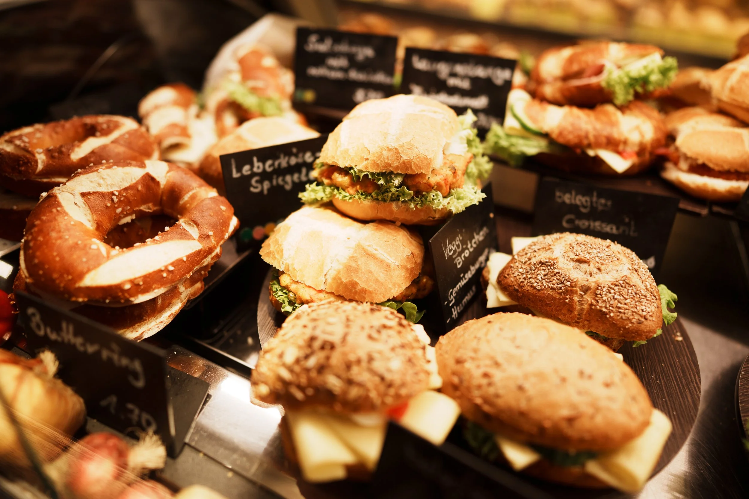 Verschiedene belegte Brötchen und Backwaren auf einem Marktstand, Beschriftungsschilder auf Deutsch.