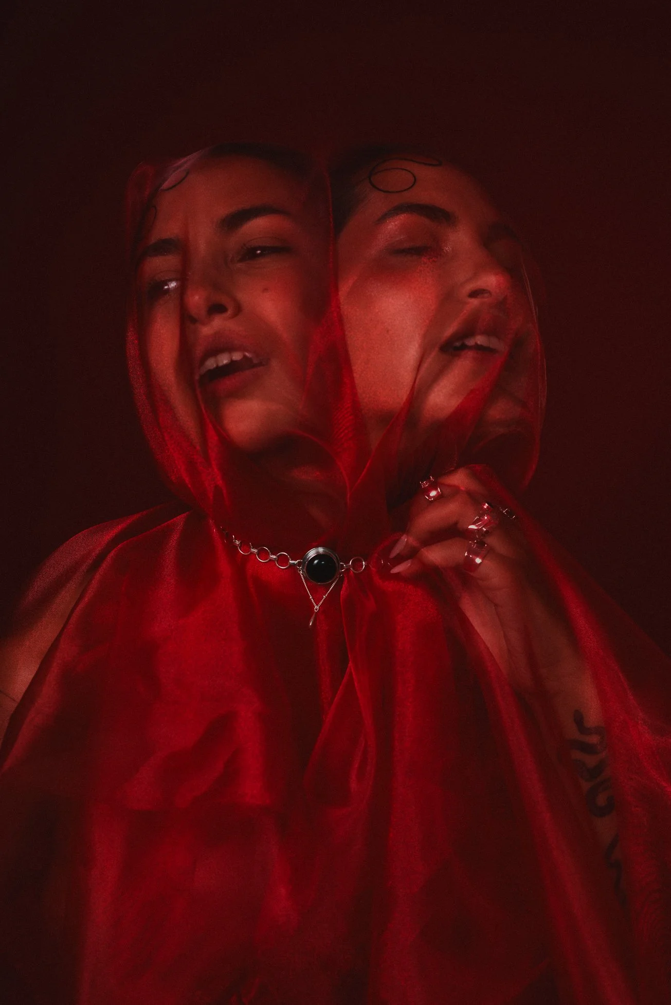 Retrato artístico de una mujer con rostro angustiado, envuelta en una tela roja y decorada con joyería, en medio de una atmósfera oscura y misteriosa.