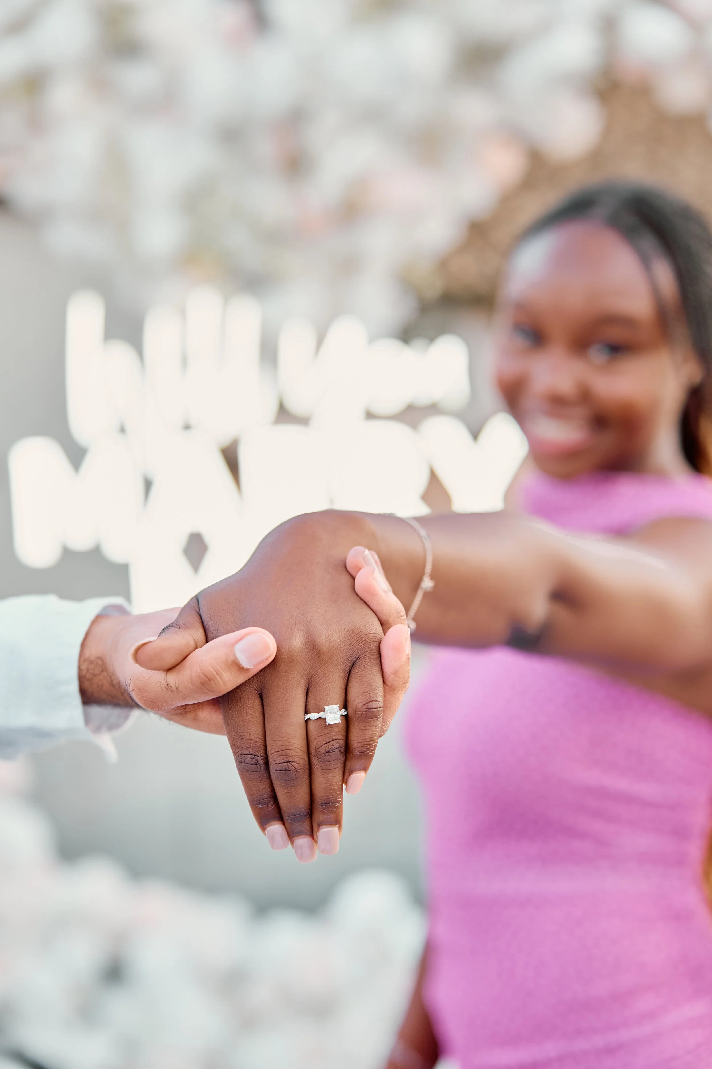 A woman and a man holding hands with the woman's hand showcasing a diamond engagement ring.