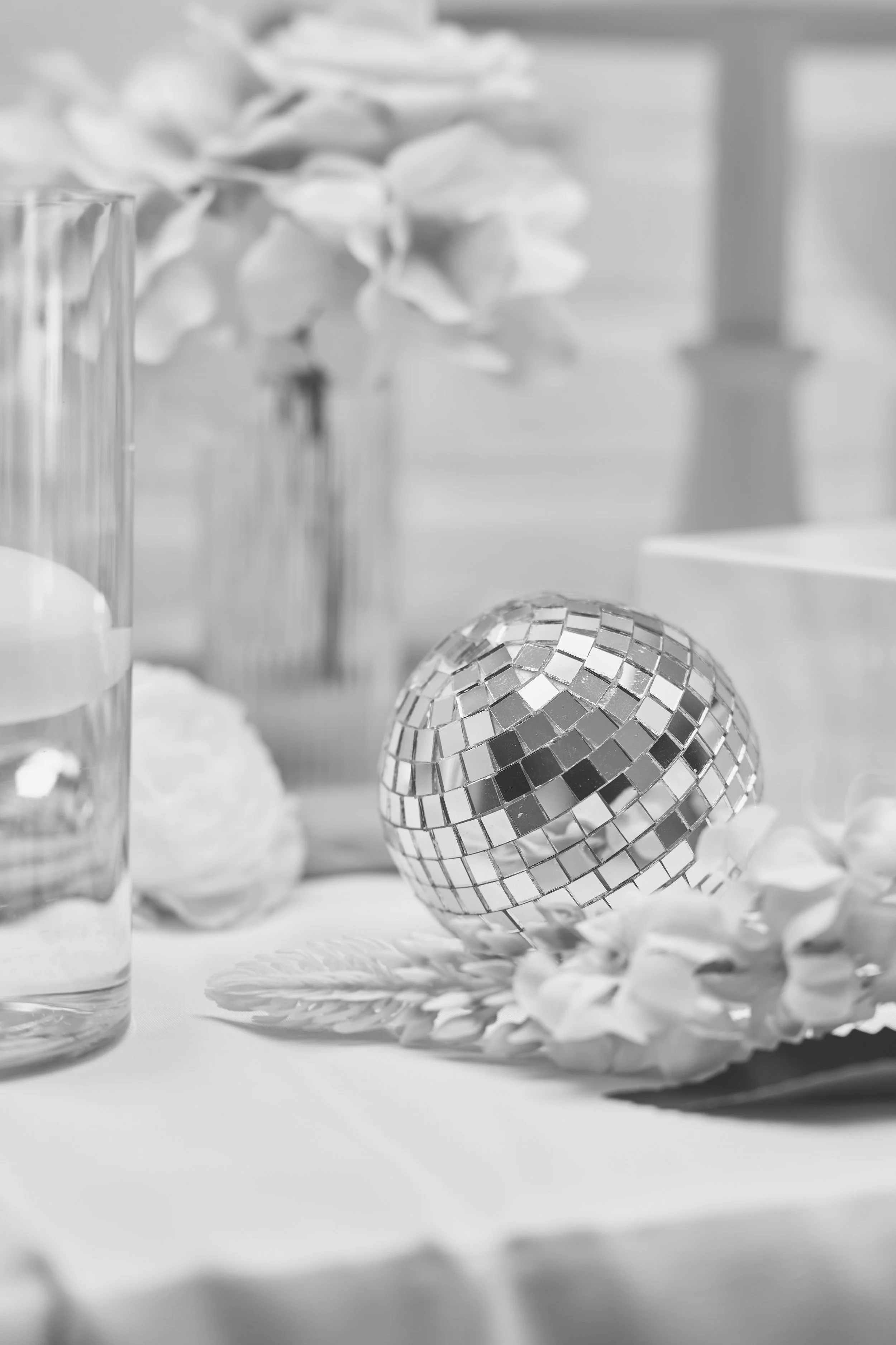 Decorative table setting with a disco ball, flowers, and a glass of water in black and white.