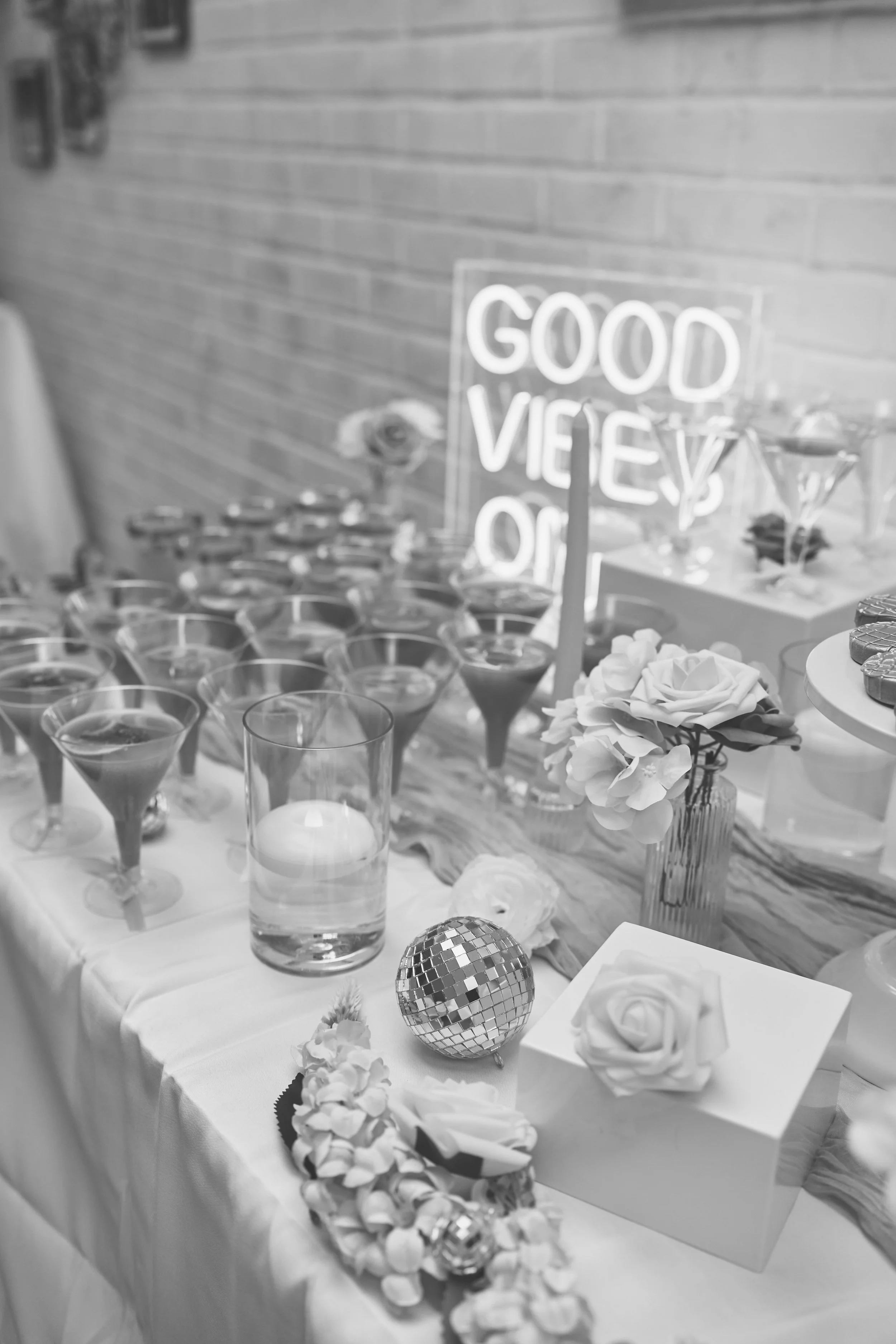 Decorative table setting with flowers, a mirror ball, candles, and a neon sign that reads 'Good Vibes Only'.