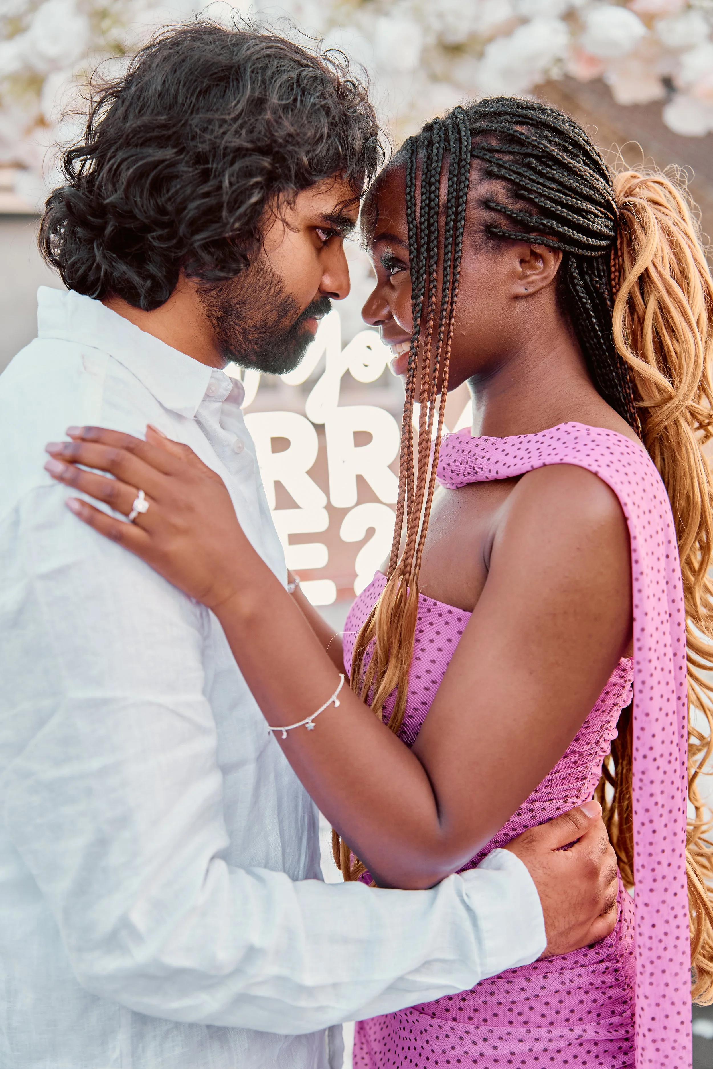 A man and woman face each other closely, their foreheads touching, as the woman gently rests her hand on the man's shoulder and the man holds her waist.