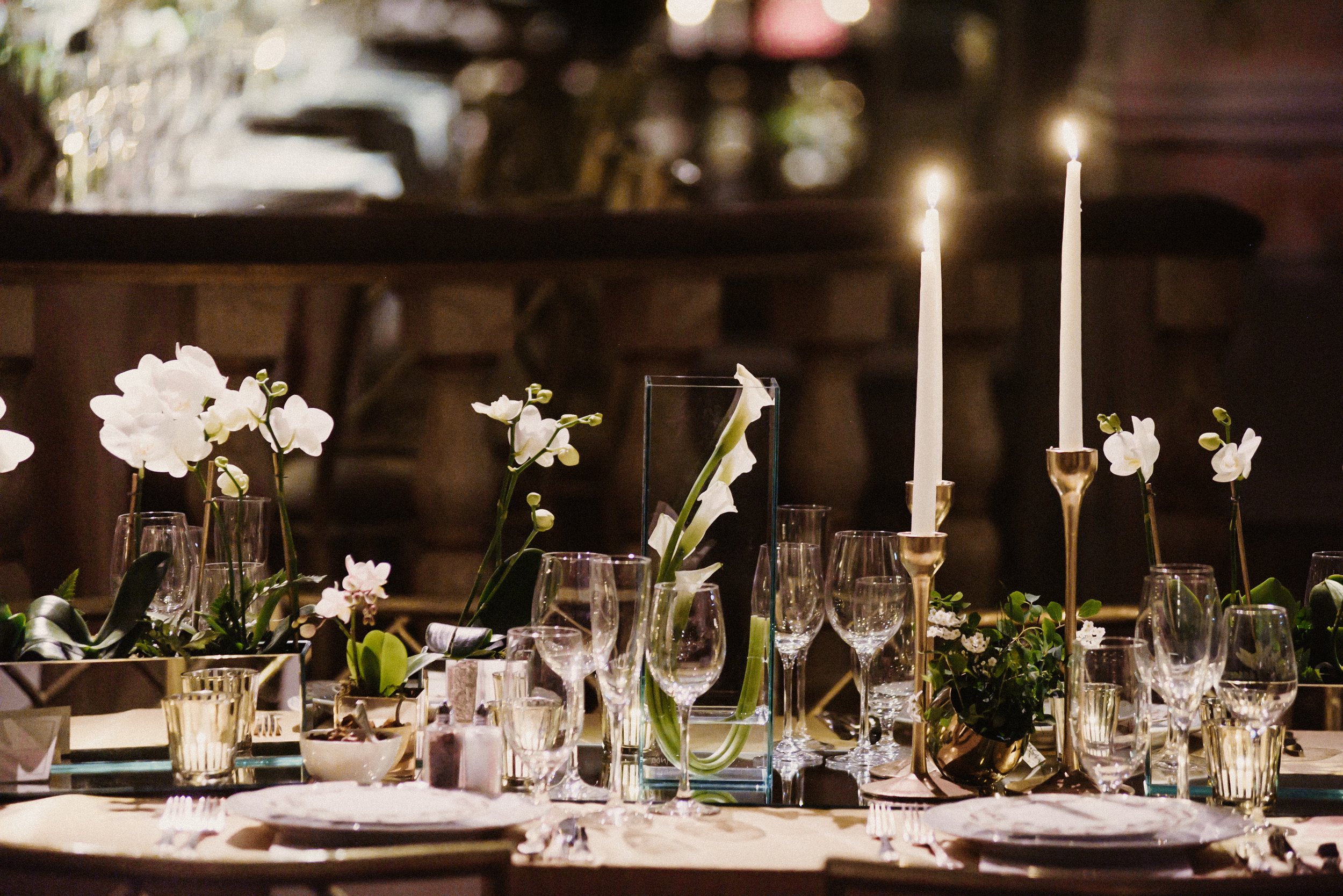 Elegant table setting with white orchids, candles, and glassware for a formal event.