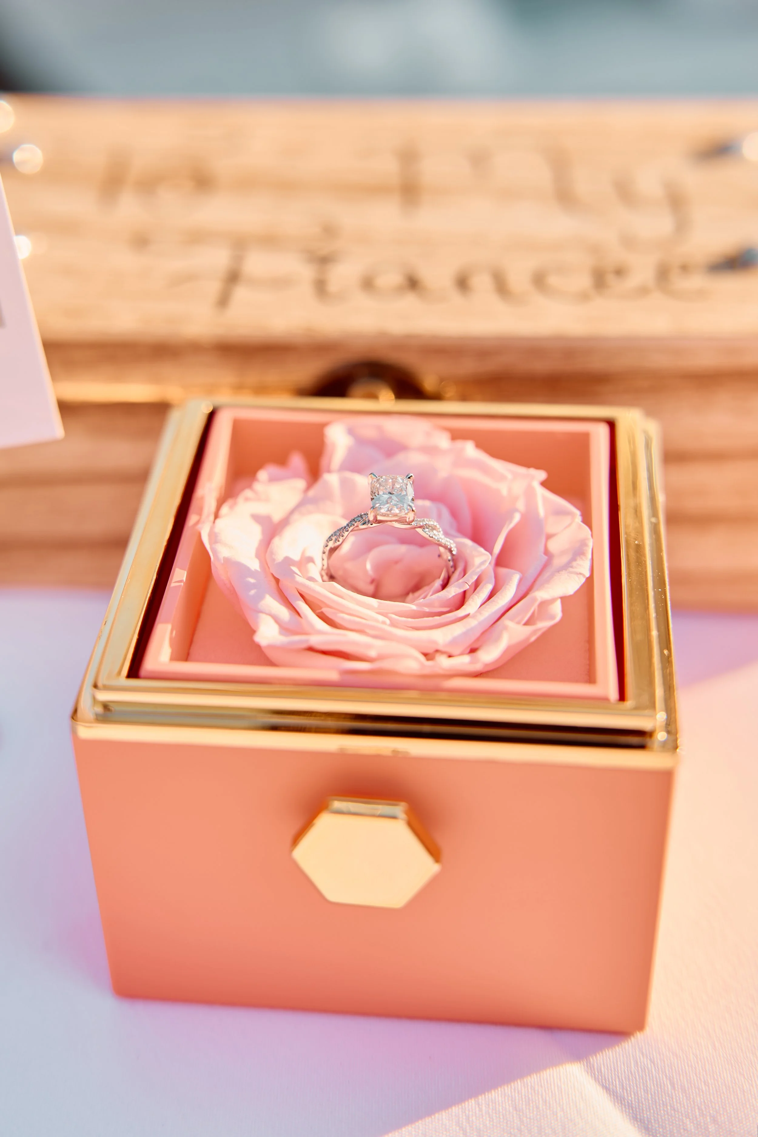 An engagement ring with a large rectangular diamond in a pink box with a pink rose inside.