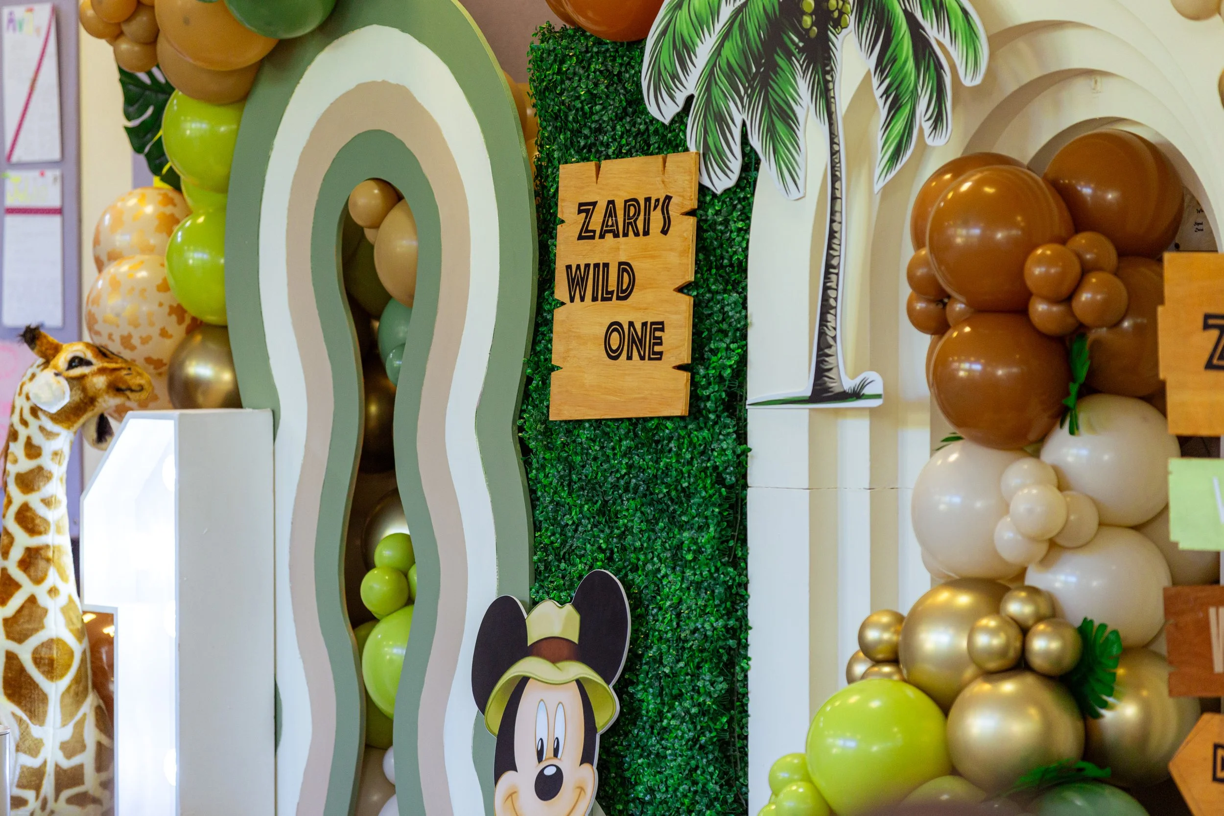 Safari themed backdrop with mickey mouse cut off, balloons and stuffed animals