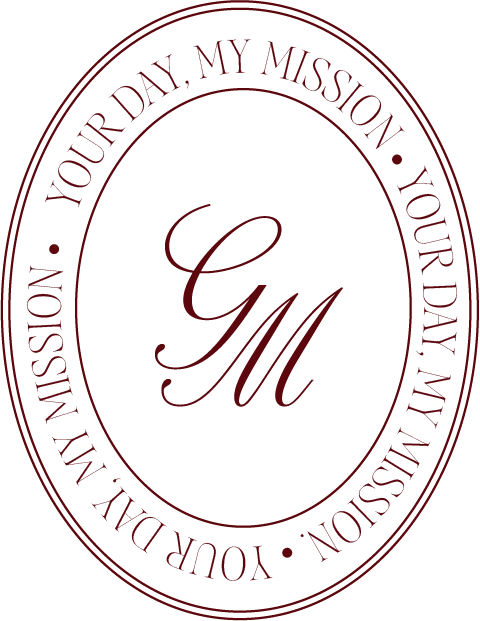 A black oval emblem with a red outline and text that reads, "Your Day, My Mission." Inside the oval, there are the initials "G M" in red, cursive font.
