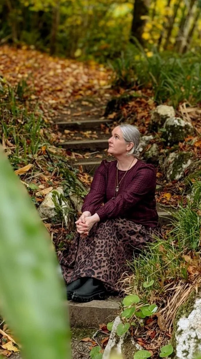 Ciara sitting on outdoor steps surrounded by autumn leaves in a forest setting.