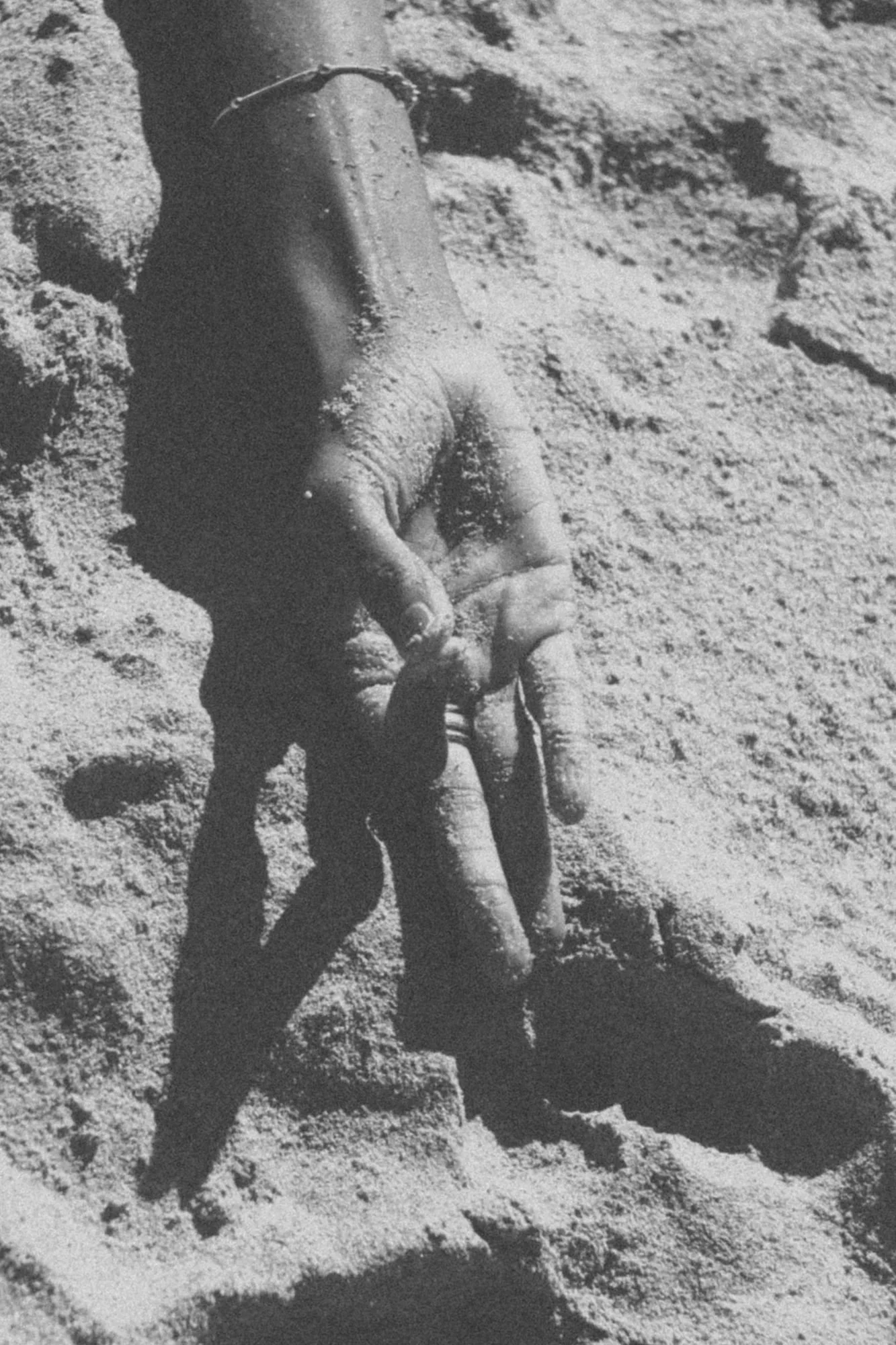 A human hand in mudra. partially buried in the sand, with fingers relaxed and palm partially visible.