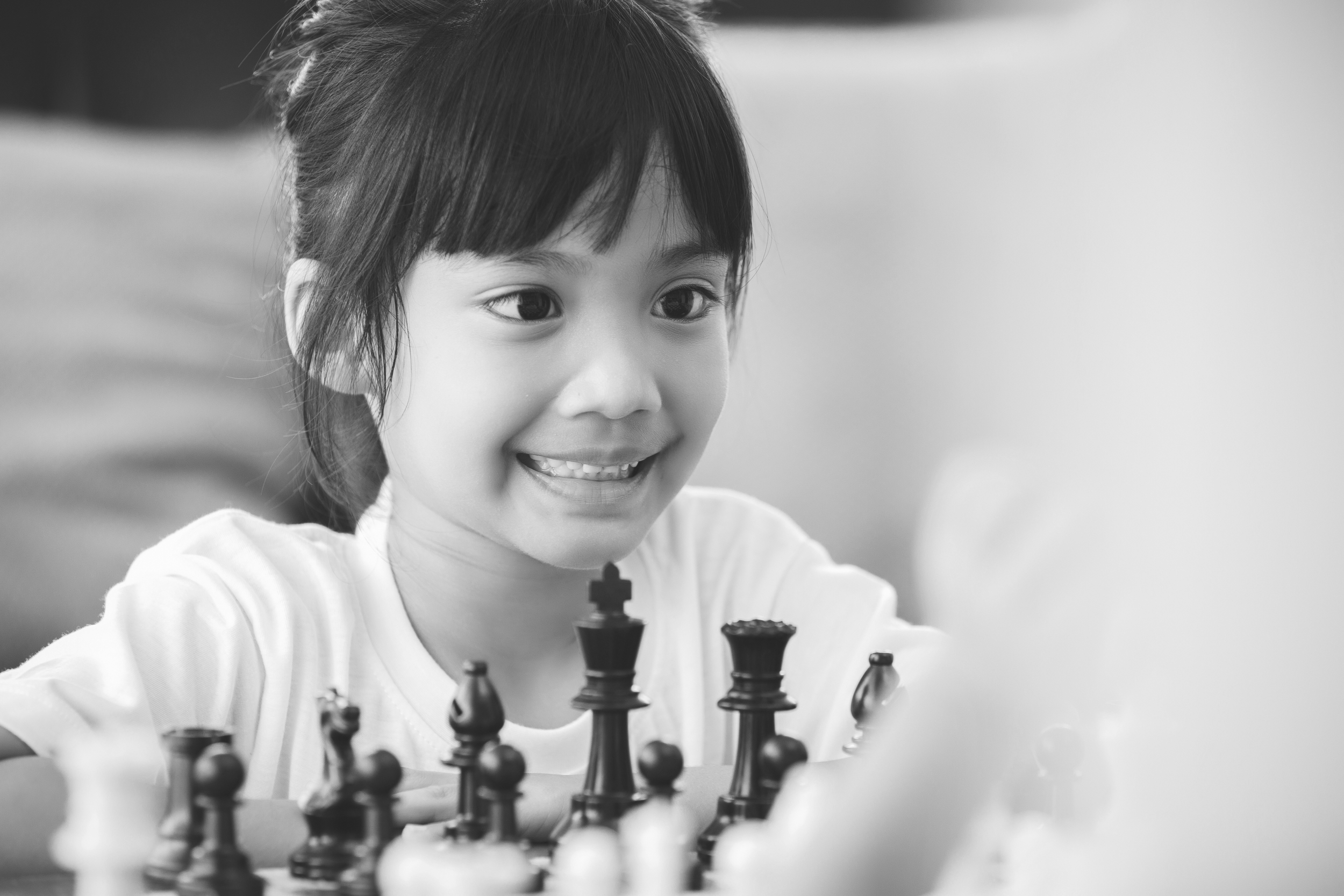 A young girl playing chess, smiling and looking at the game pieces.
