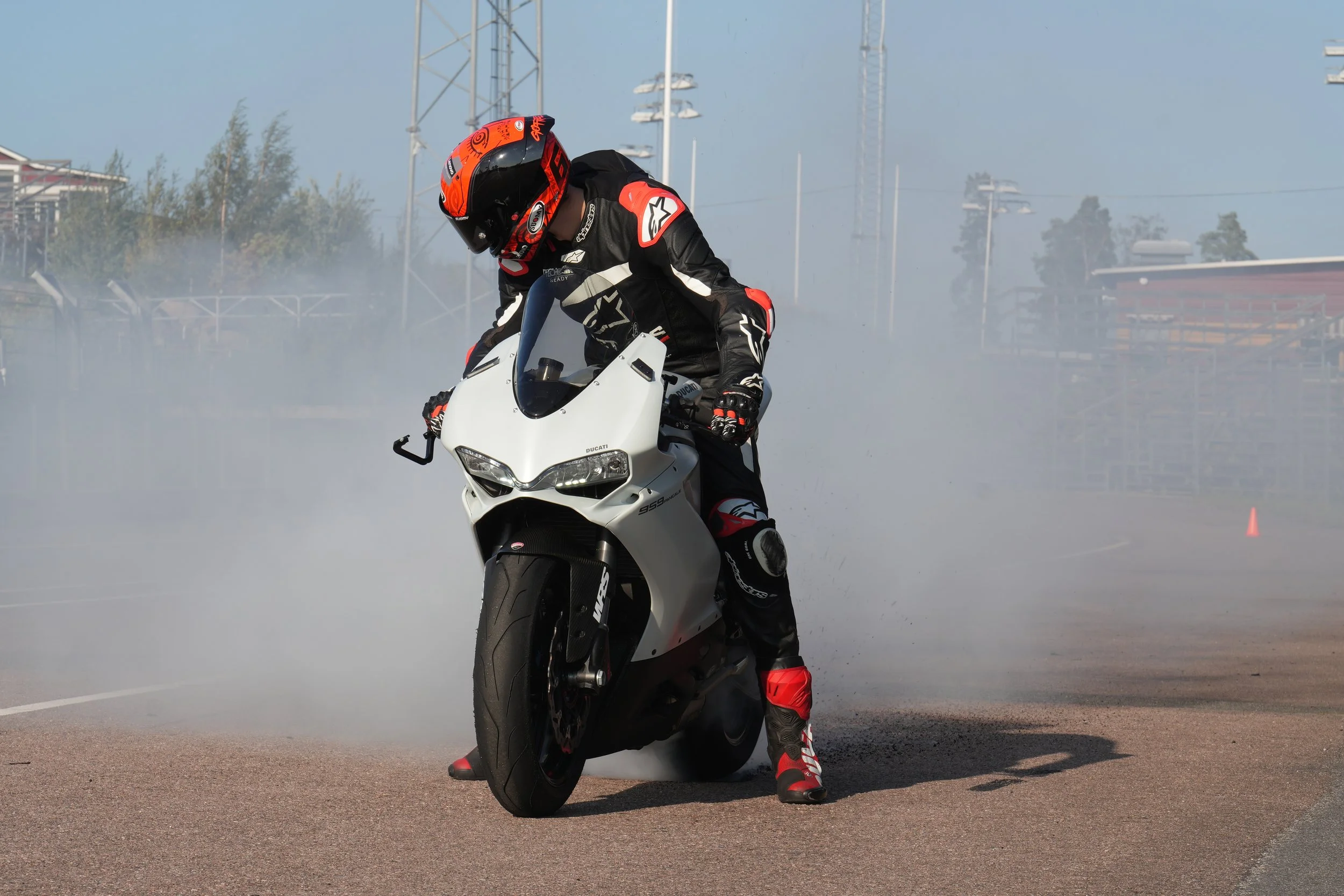 Motorcycle rider doing a burnout on a white Ducati sportbike, surrounded by smoke on a racetrack