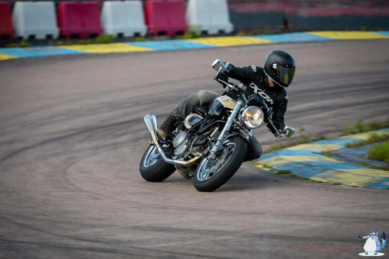 Motorcycle rider leaning into a turn on a racetrack wearing black helmet and gear.