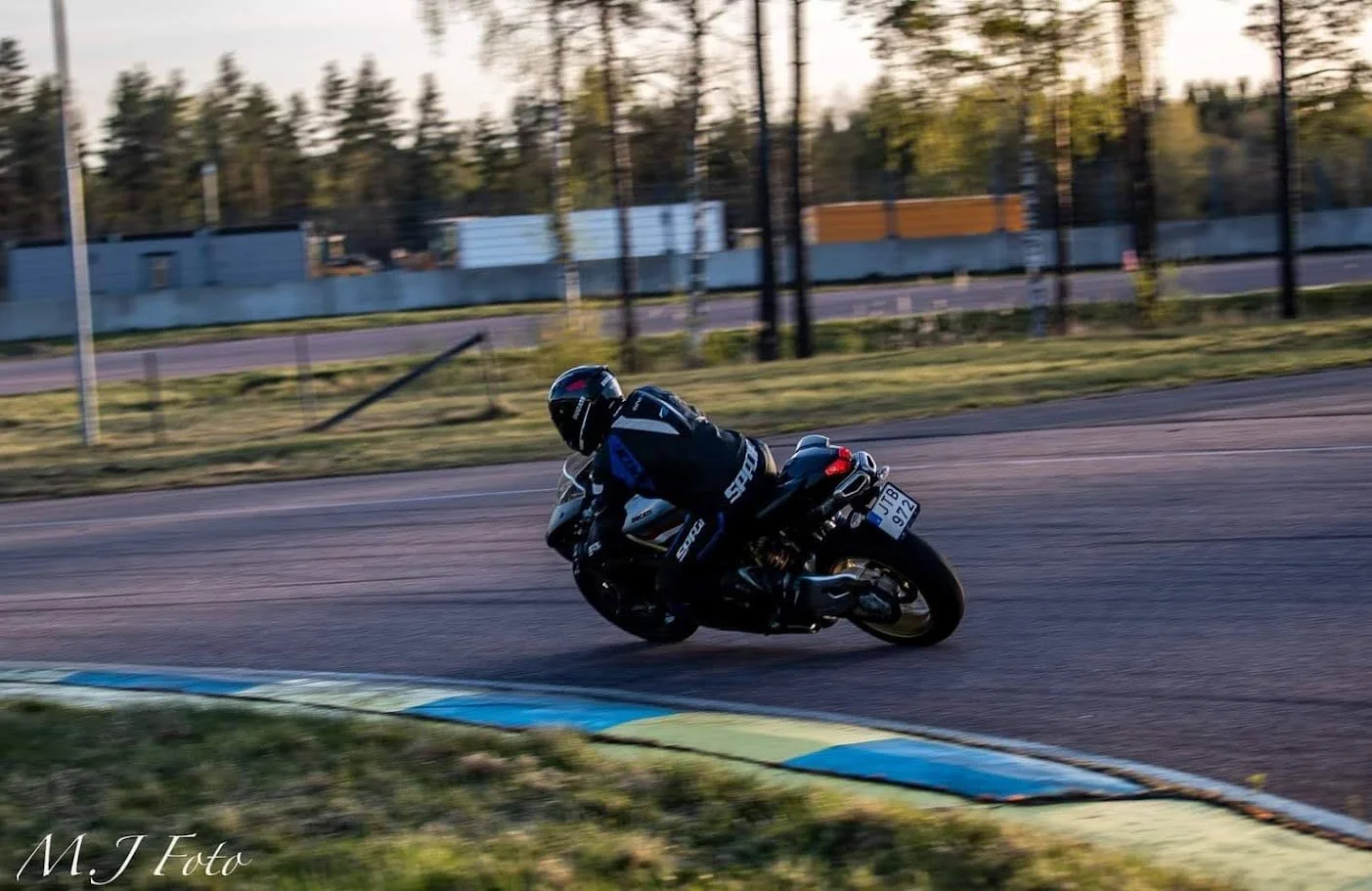 Motorcycle racer in black and blue gear rounding a curve on a race track at sunset.