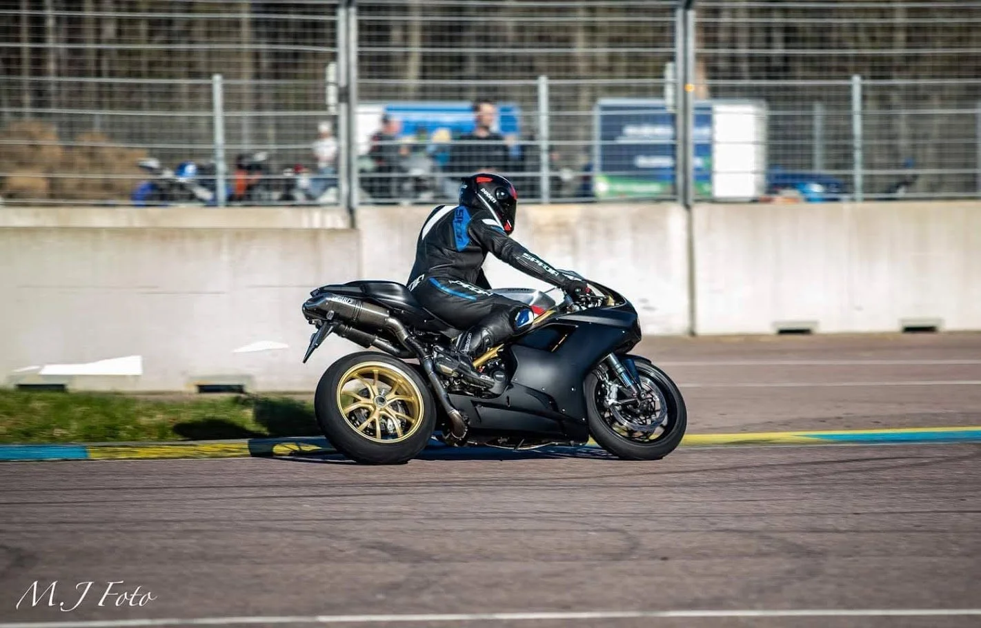A motorcyclist in racing gear riding a black motorcycle on a racetrack.