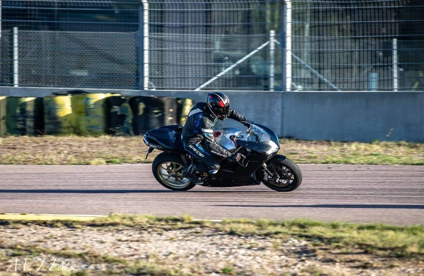 Motorcycle racer in black and blue gear riding a black motorcycle on a race track.