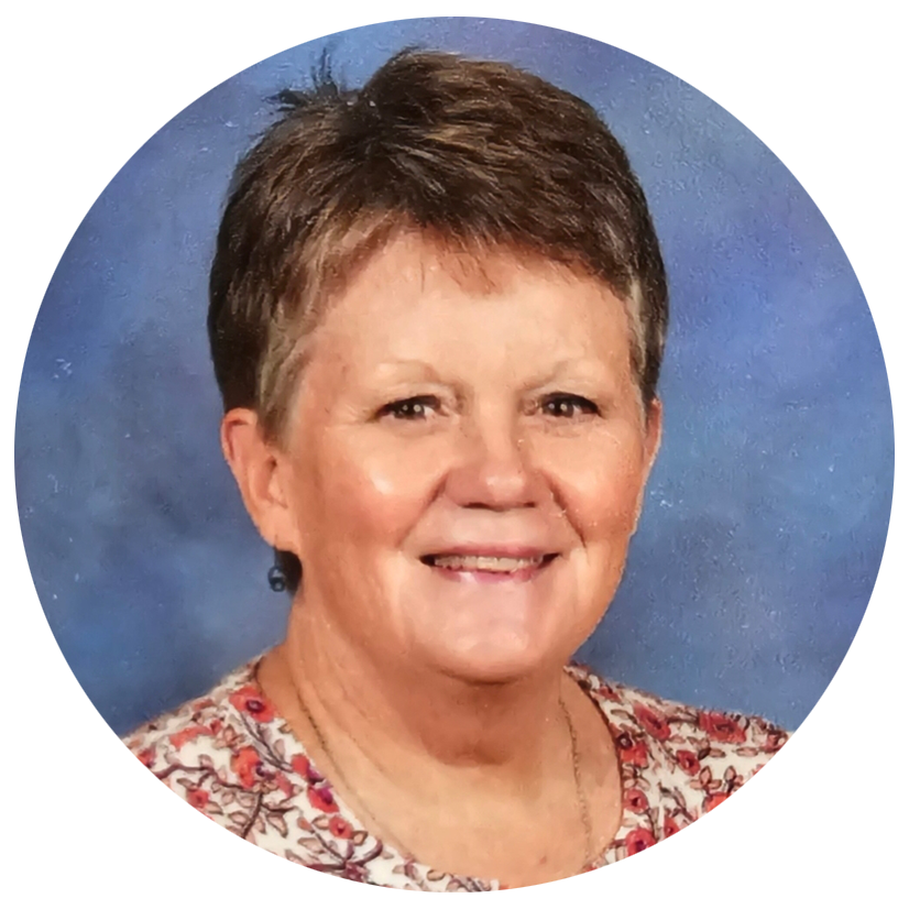 A smiling middle-aged woman with short brown hair, wearing a floral patterned blouse, against a blue background.