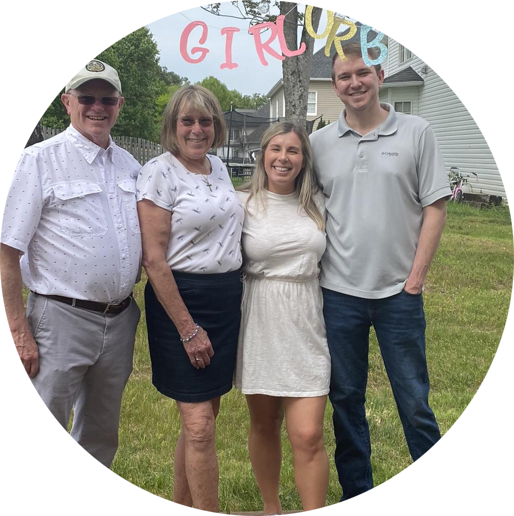 Four people standing outdoors in a yard, smiling, with a house and trees in the background. A colorful sign spelling 'GIRL CURL' is hanging above them.