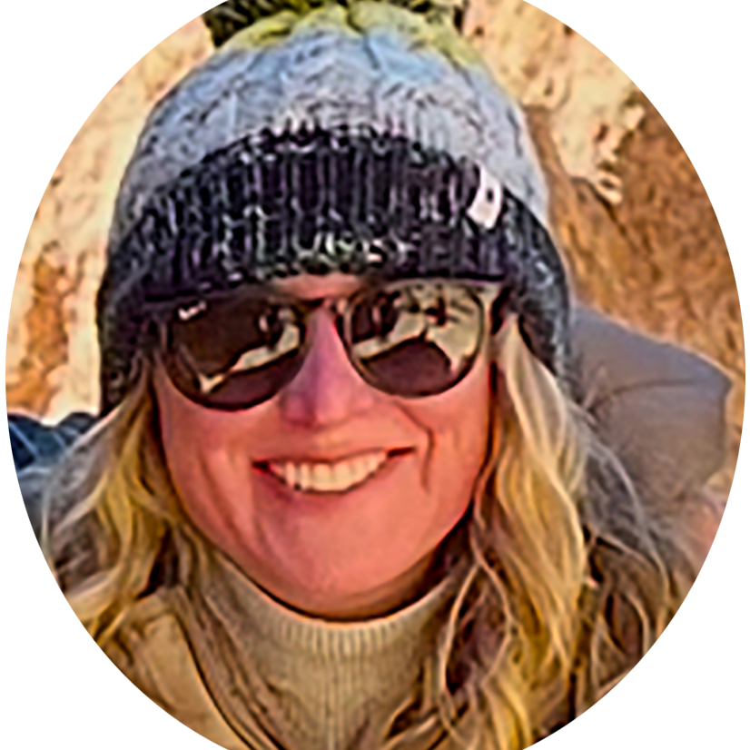 Woman smiling outdoors wearing sunglasses, a knitted beanie, and a beige turtleneck in a natural setting.