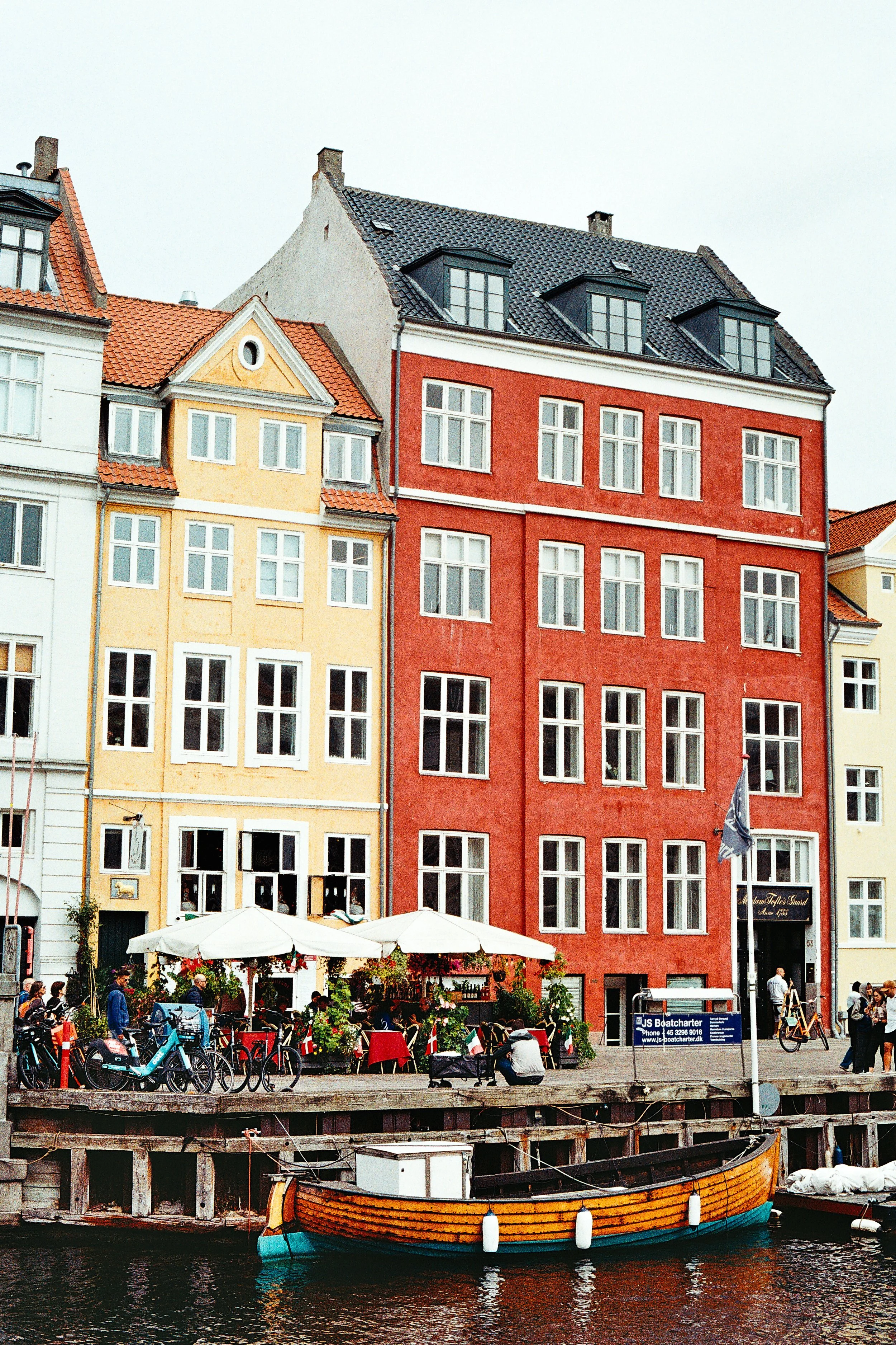 Colorful buildings along a waterfront with bicycles, outdoor seating, and a boat in the foreground.