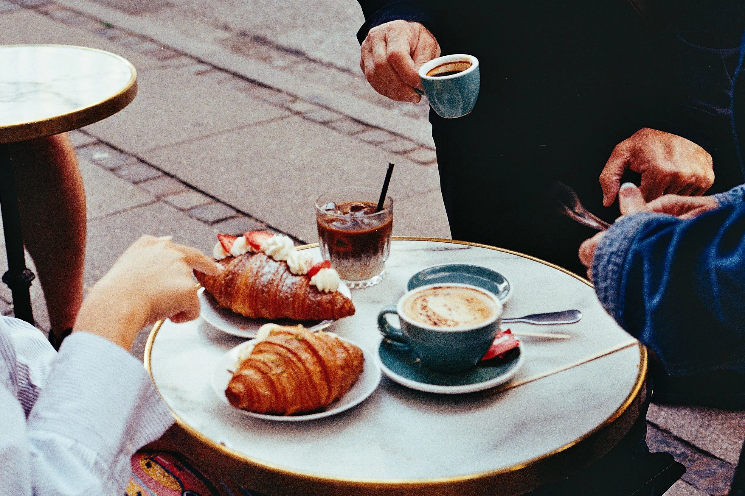 People sharing coffee and croissants at an outdoor cafe table