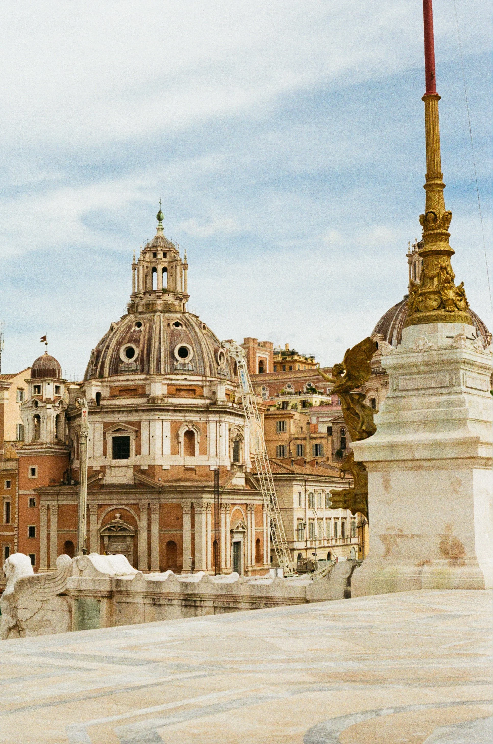 View of the rooftops and domes of historic buildings in Rome, Italy, with a partly cloudy sky in the background.