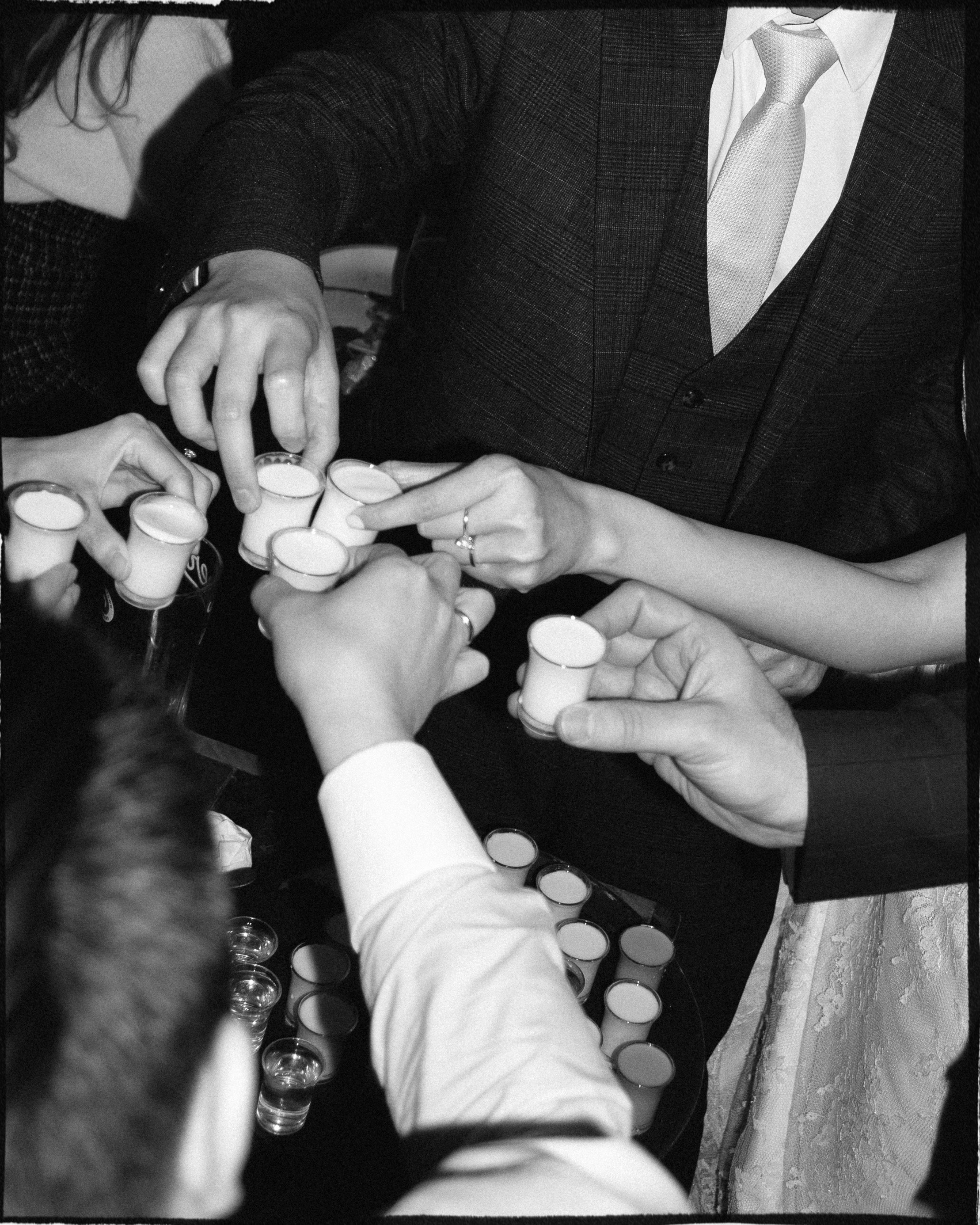 Group of people clinking shot glasses filled with a drink at a celebration or gathering.