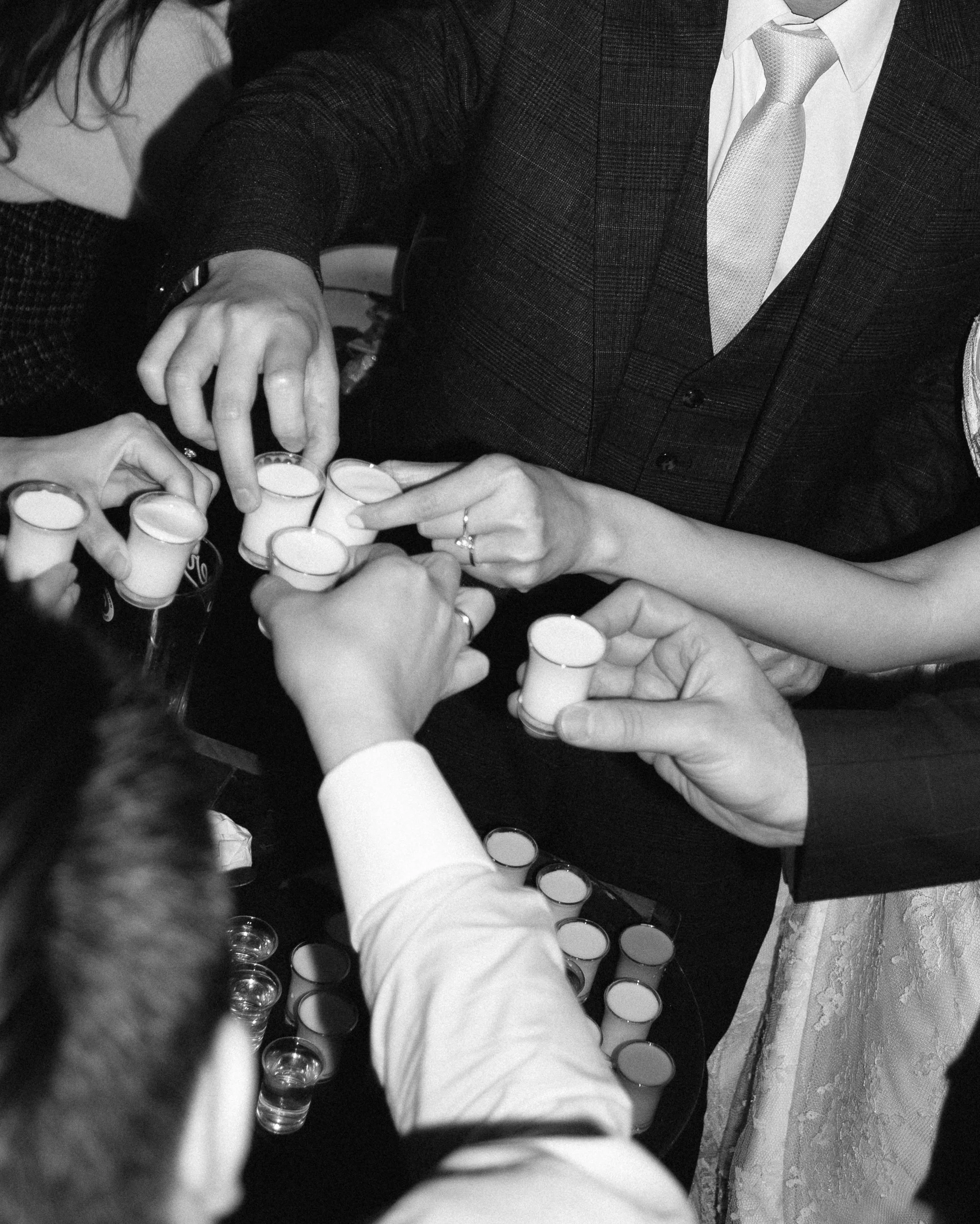 Several people gathered around a table, clinking shot glasses filled with a beverage in a toast.
