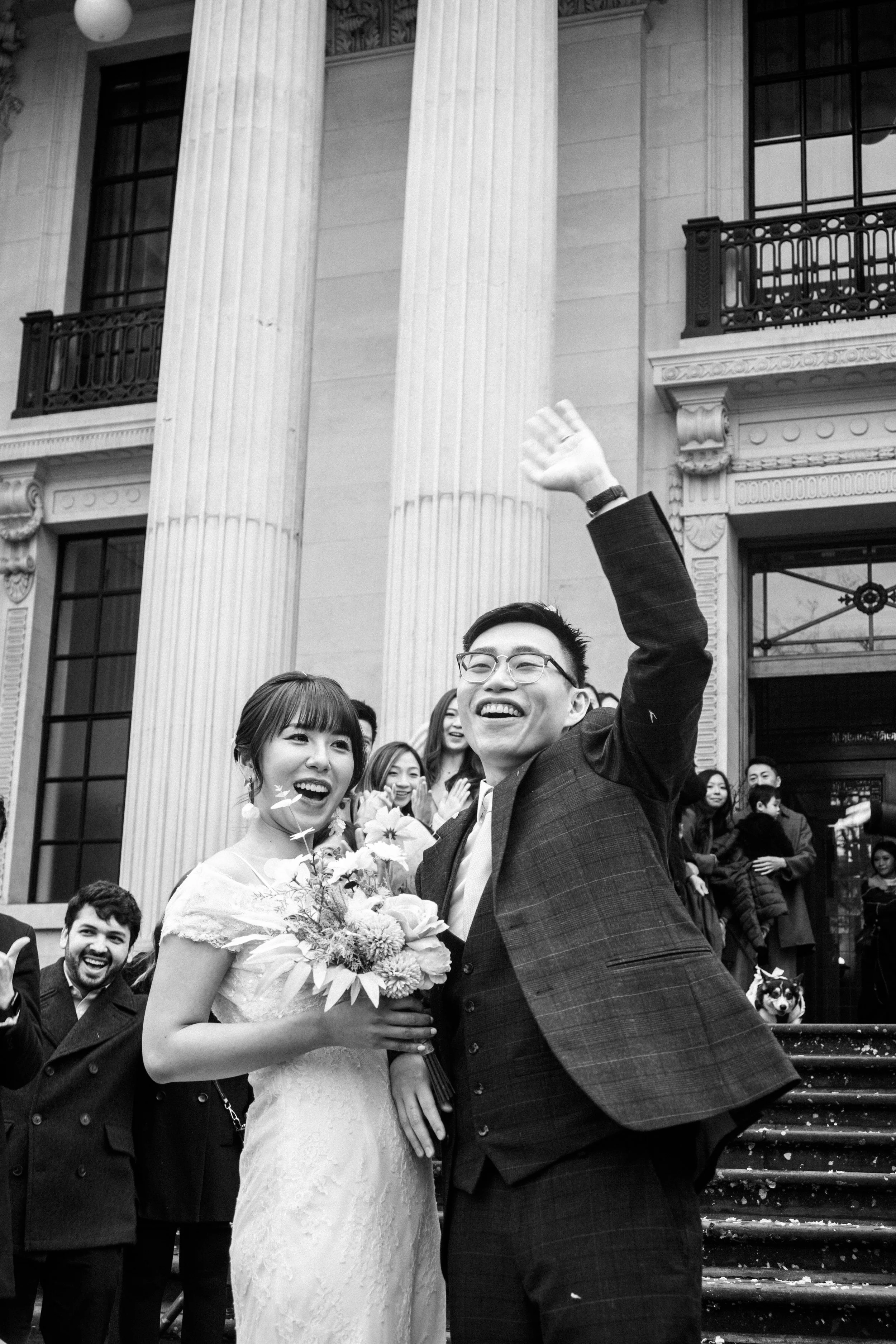 A joyful wedding celebration with a bride holding a bouquet, surrounded by friends and family, in front of a grand building with large columns.