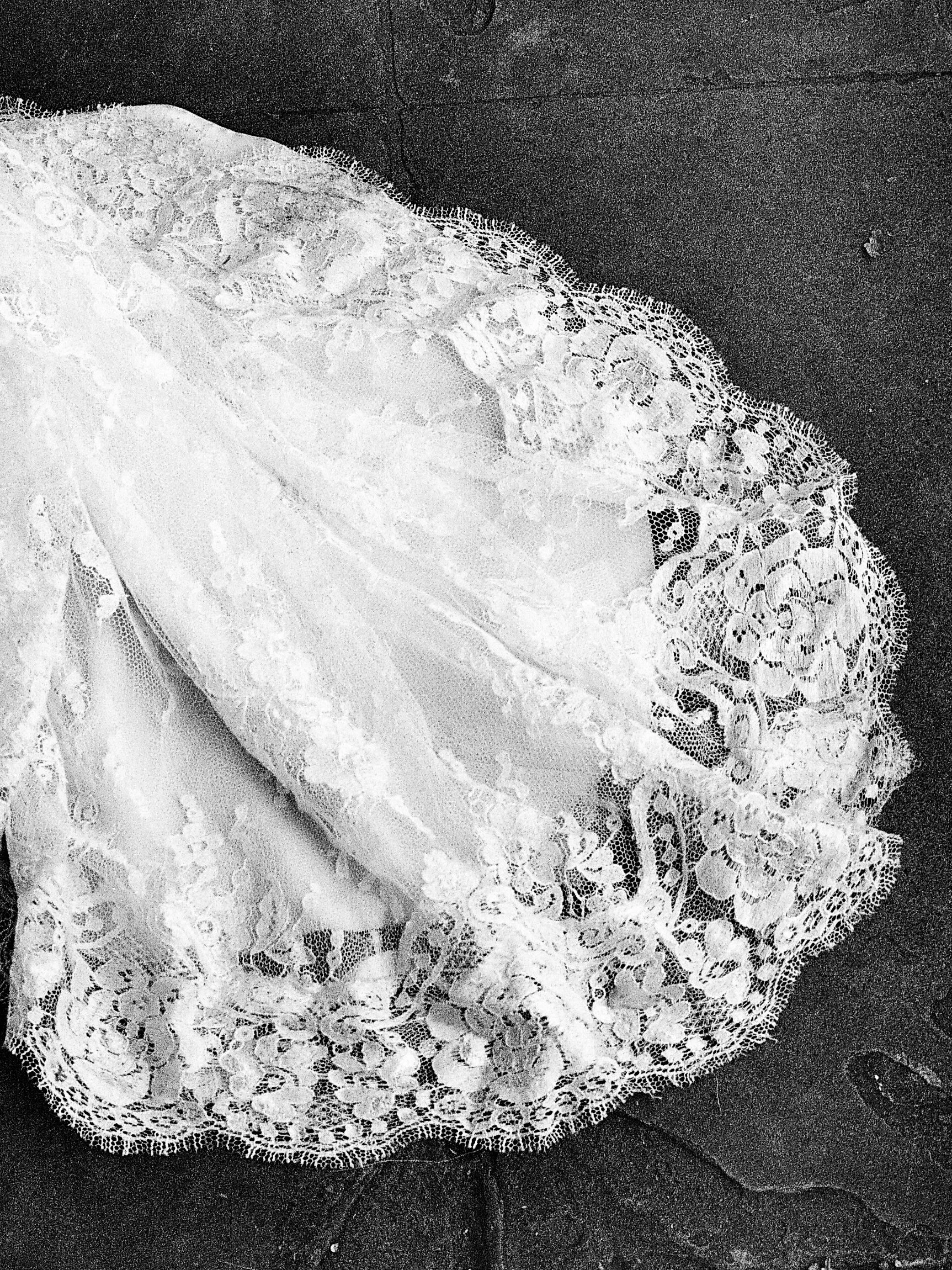 Close-up of white lace fabric with intricate floral patterns, set against a dark background.