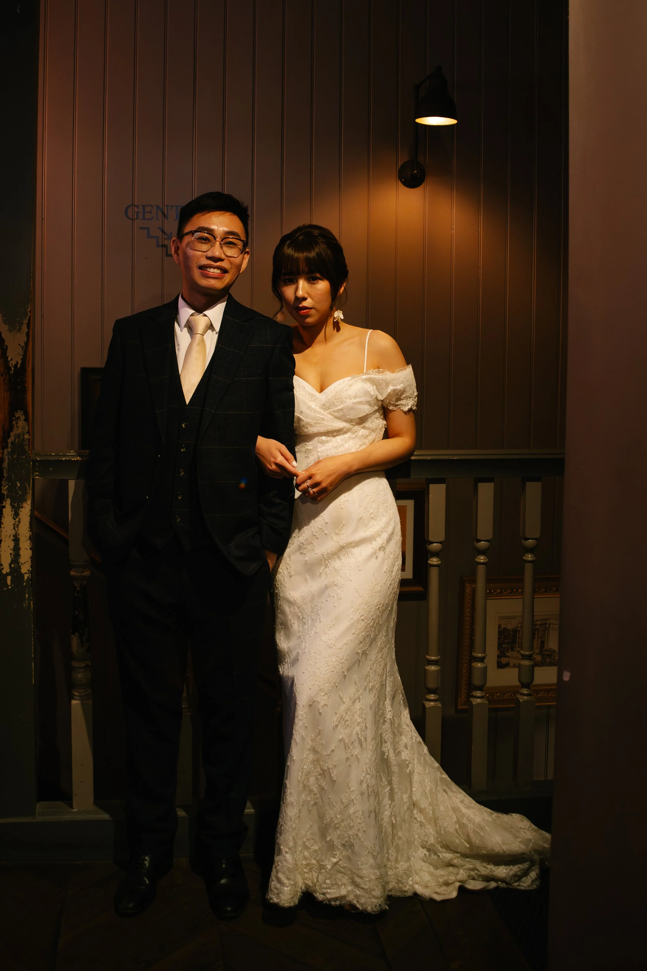 A man in a suit and a woman in a wedding dress standing together indoors at a wedding reception or event.