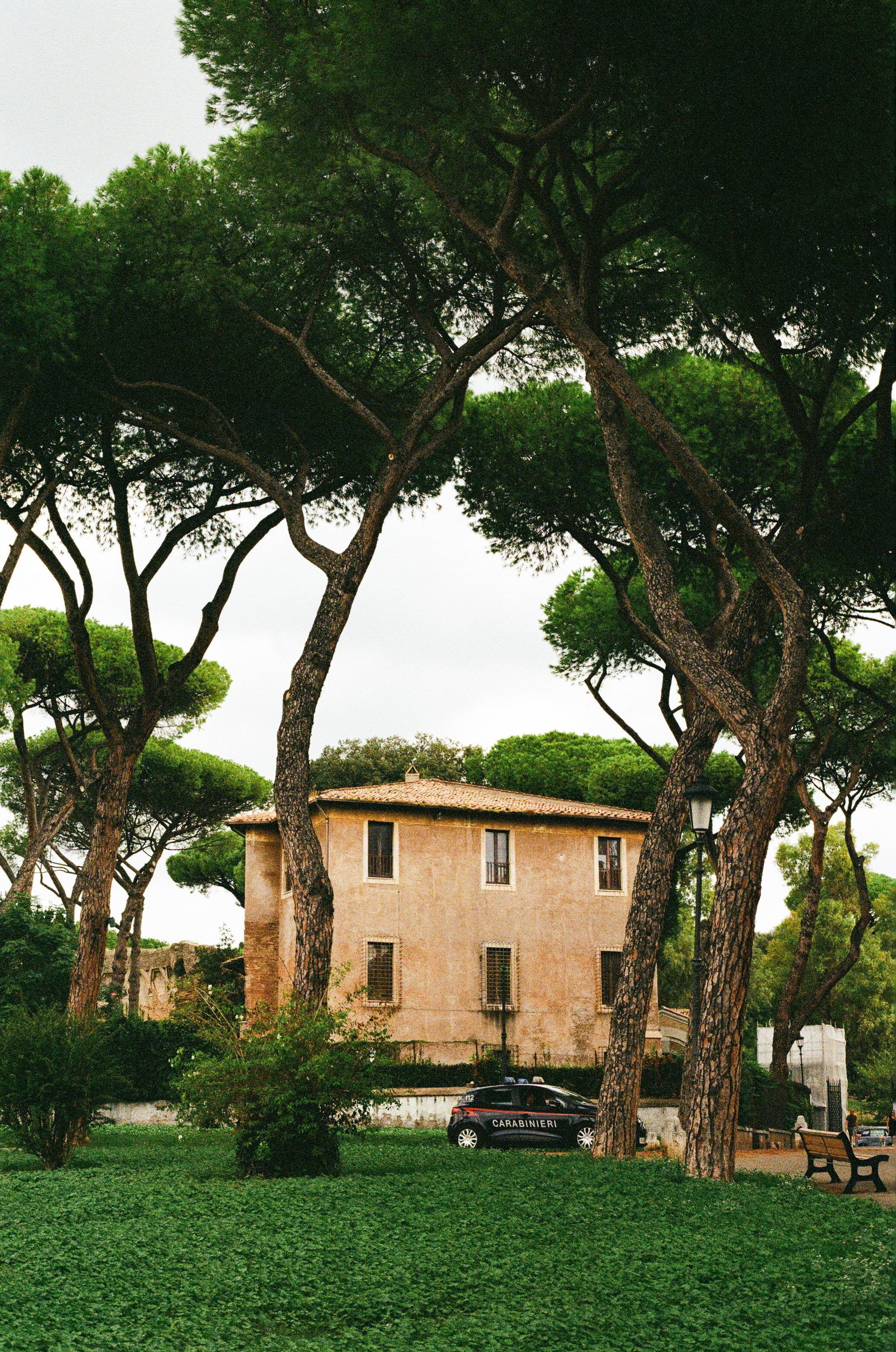 A beige two-story building surrounded by tall, green trees with a police car parked in front.