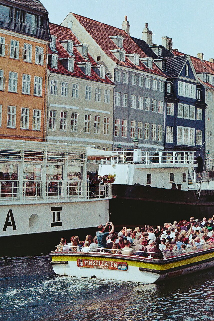 A boat filled with tourists on a canal in Copenhagen, Denmark, with colorful buildings in the background.
